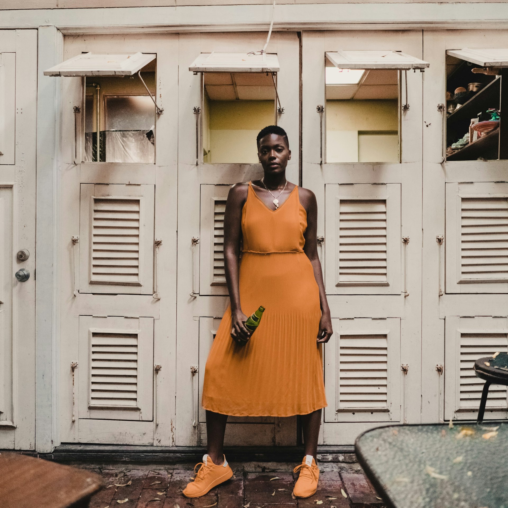 A black woman wearing an orange dress with matching sneakers poses for the camera