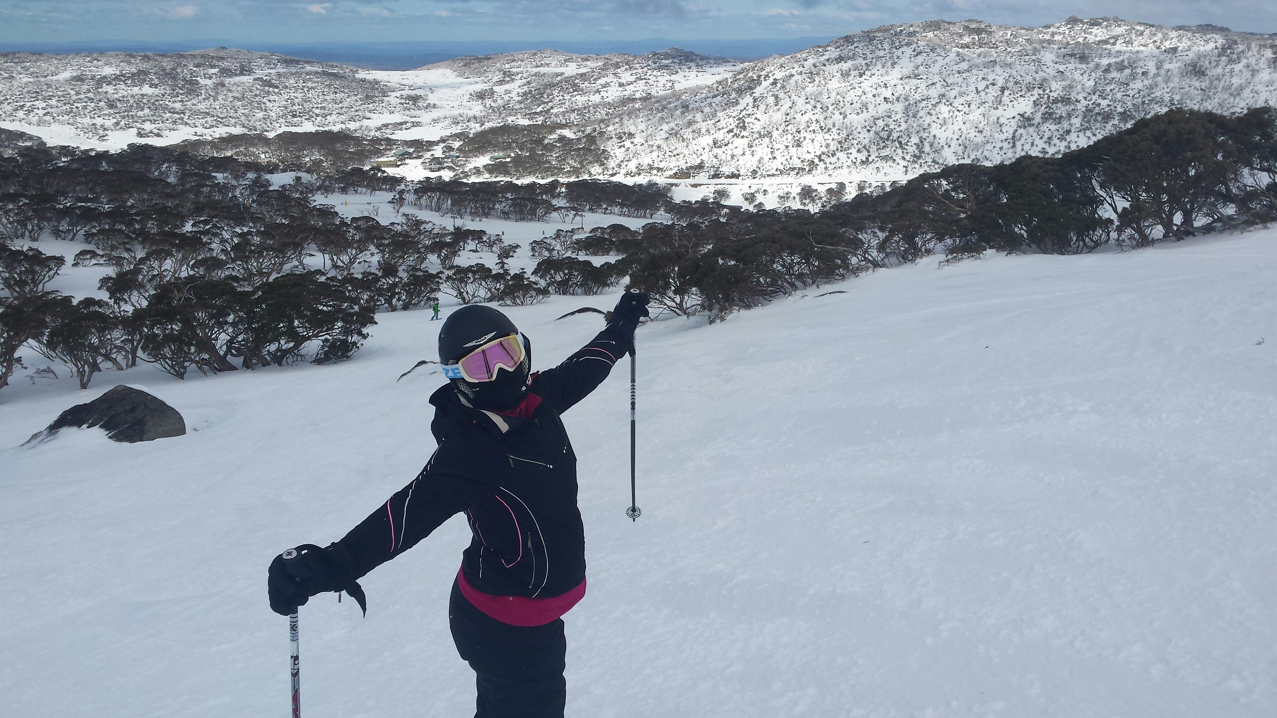 A woman in full ski gear poses for the camera with her arms out wide. She's standing on snowy slopes in Australia
