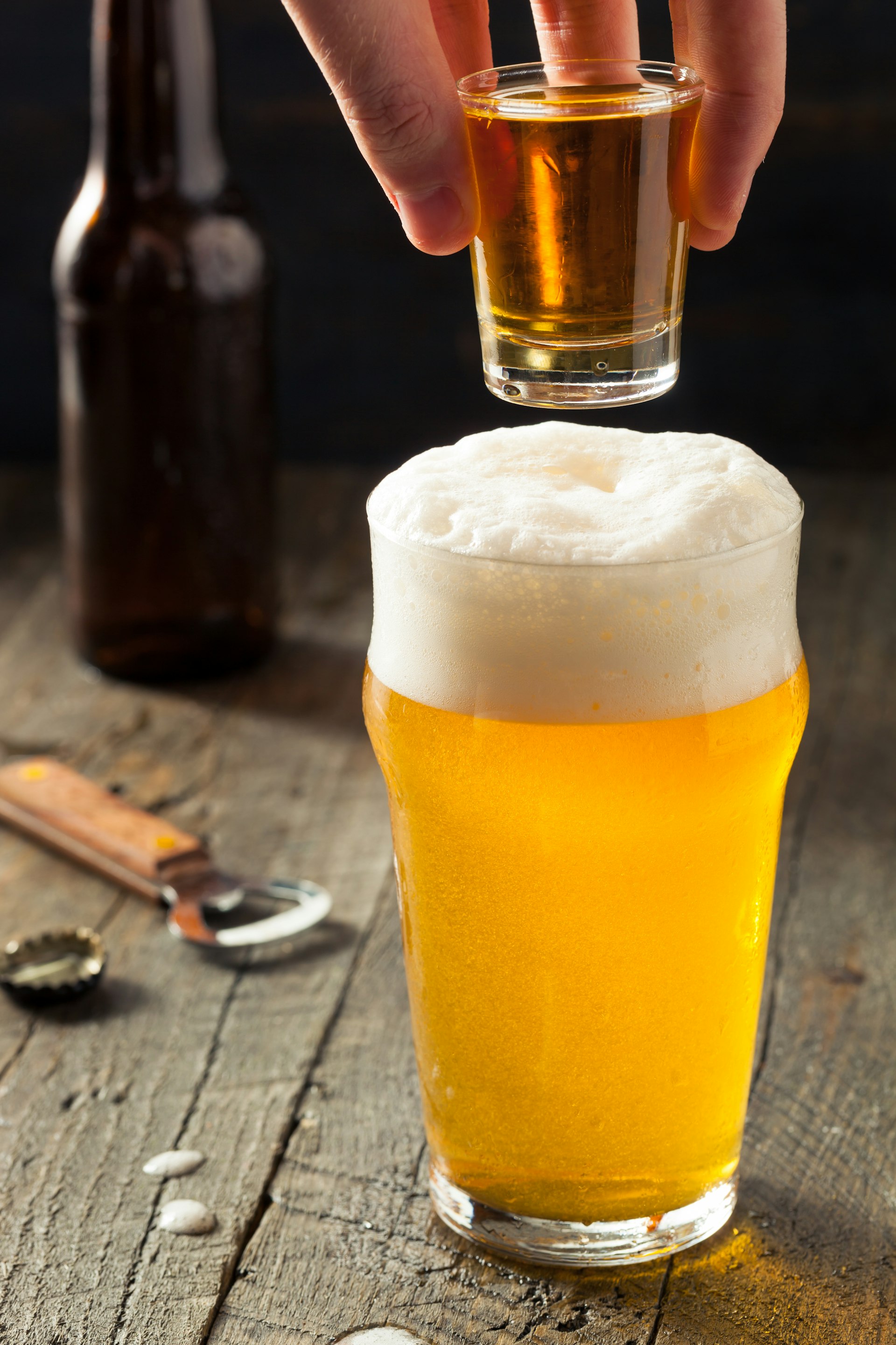 A person drops a shot of whiskey into a tall glass of beer