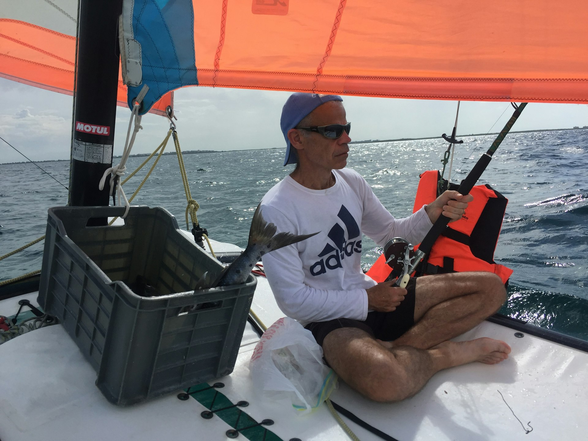 A man sitting on a sail boat with a fishing rod