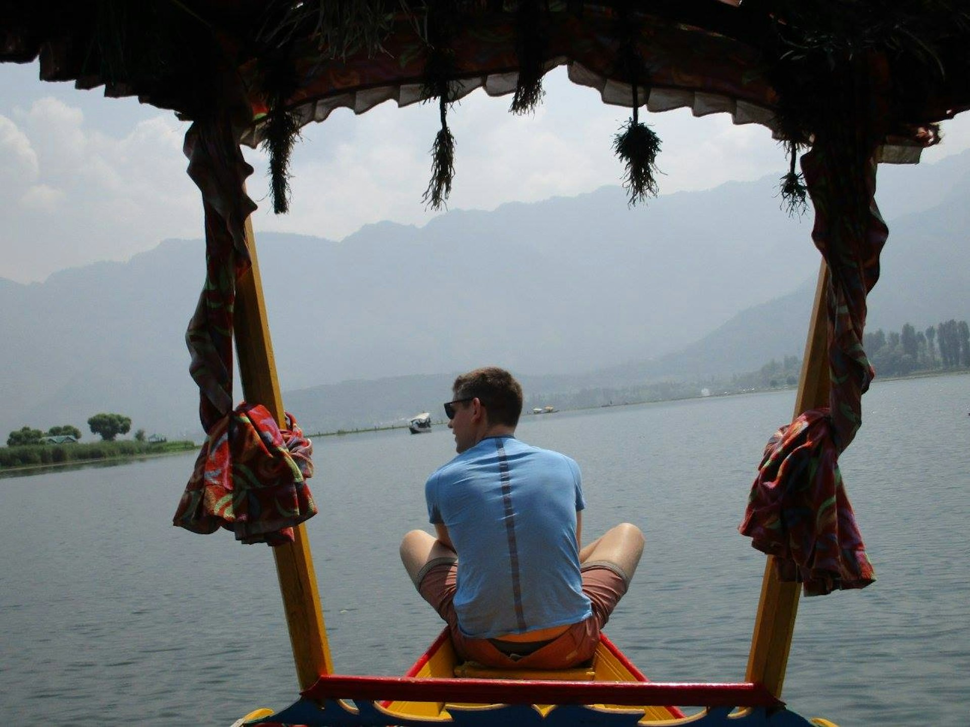 A man sits cross-legged at the prow of a small boat on a large lake