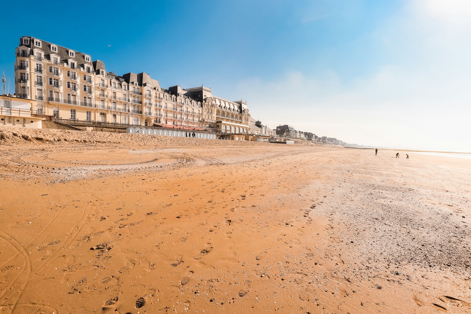A wide, empty sandy Beach with buildings dating from the early 20th century lining the seafront