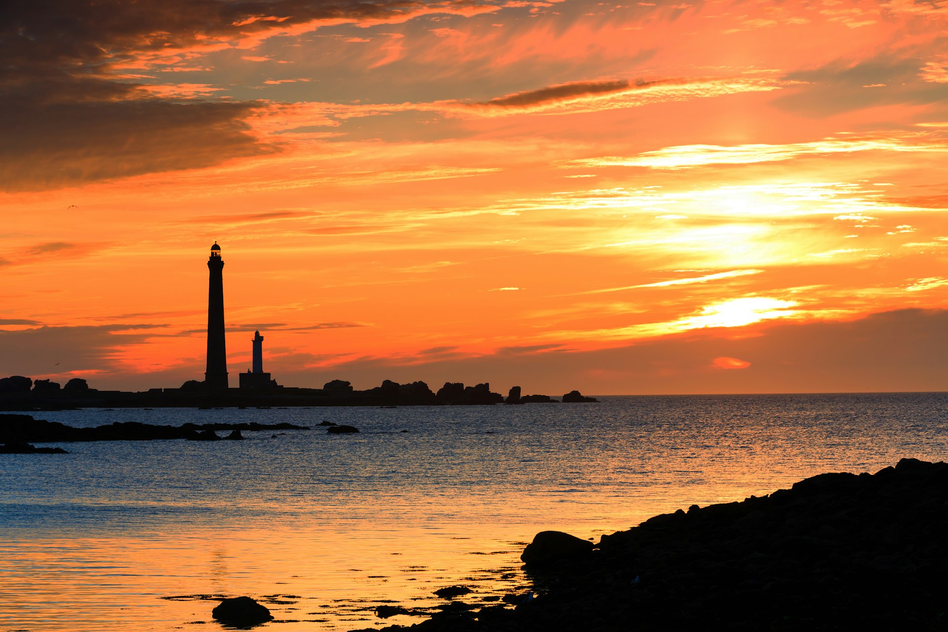 Two lighthouses, one significantly taller than the other, are silhouetted at sunset
