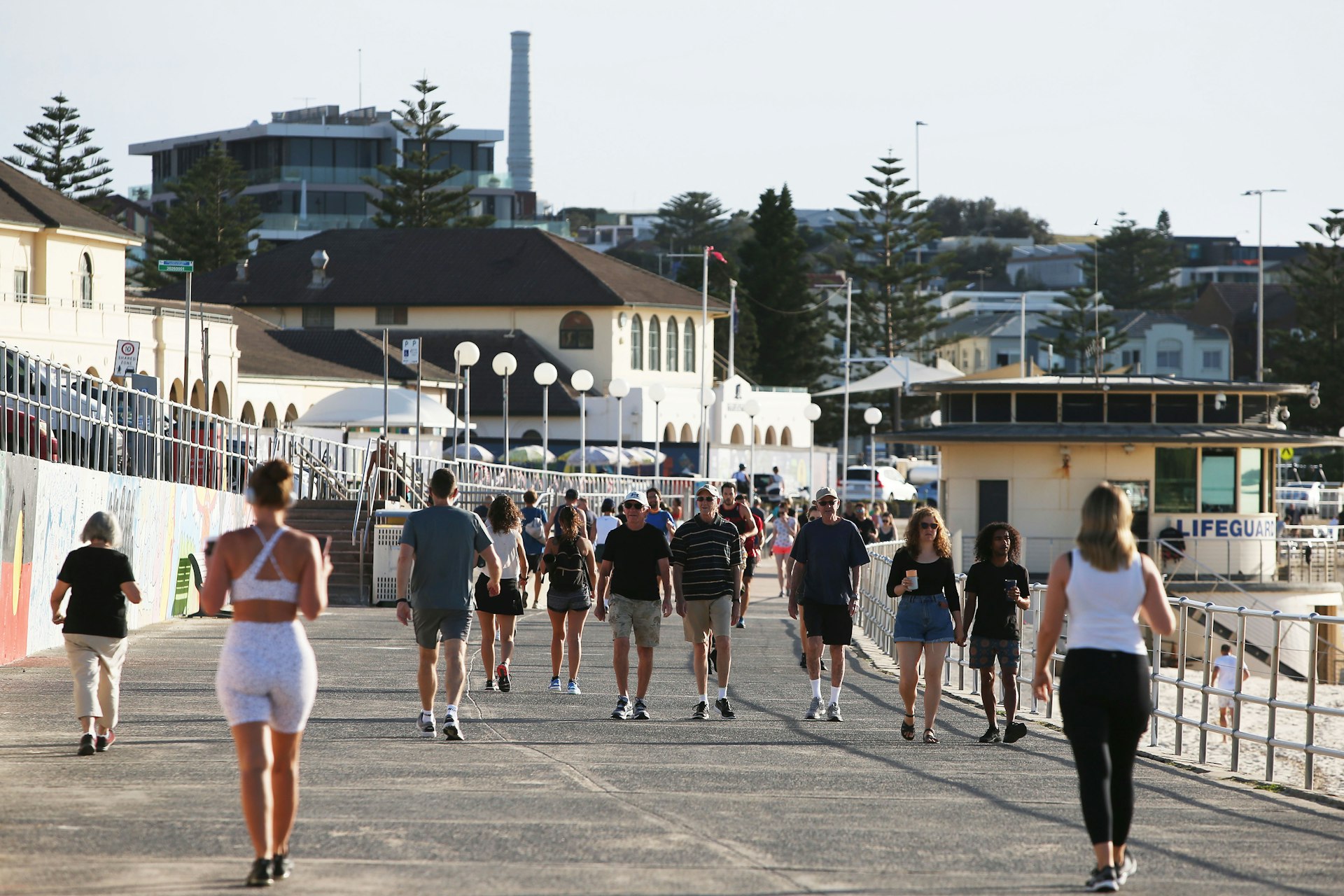 People, wearing summer gear, walk a path alongside a beach solo or in small groups 