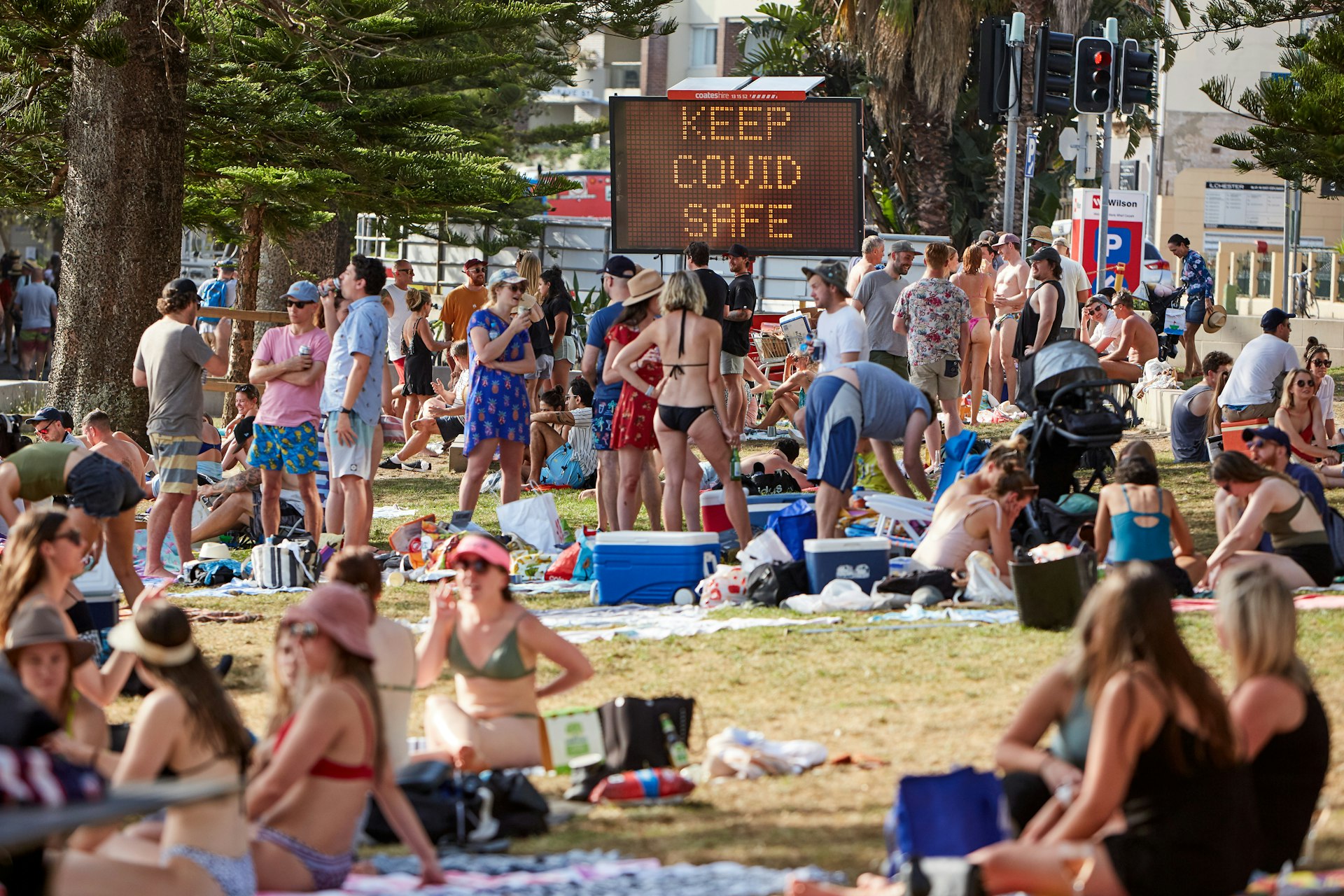A busy beach in Australia, with a digital sign in the background saying "Keep COVID safe"