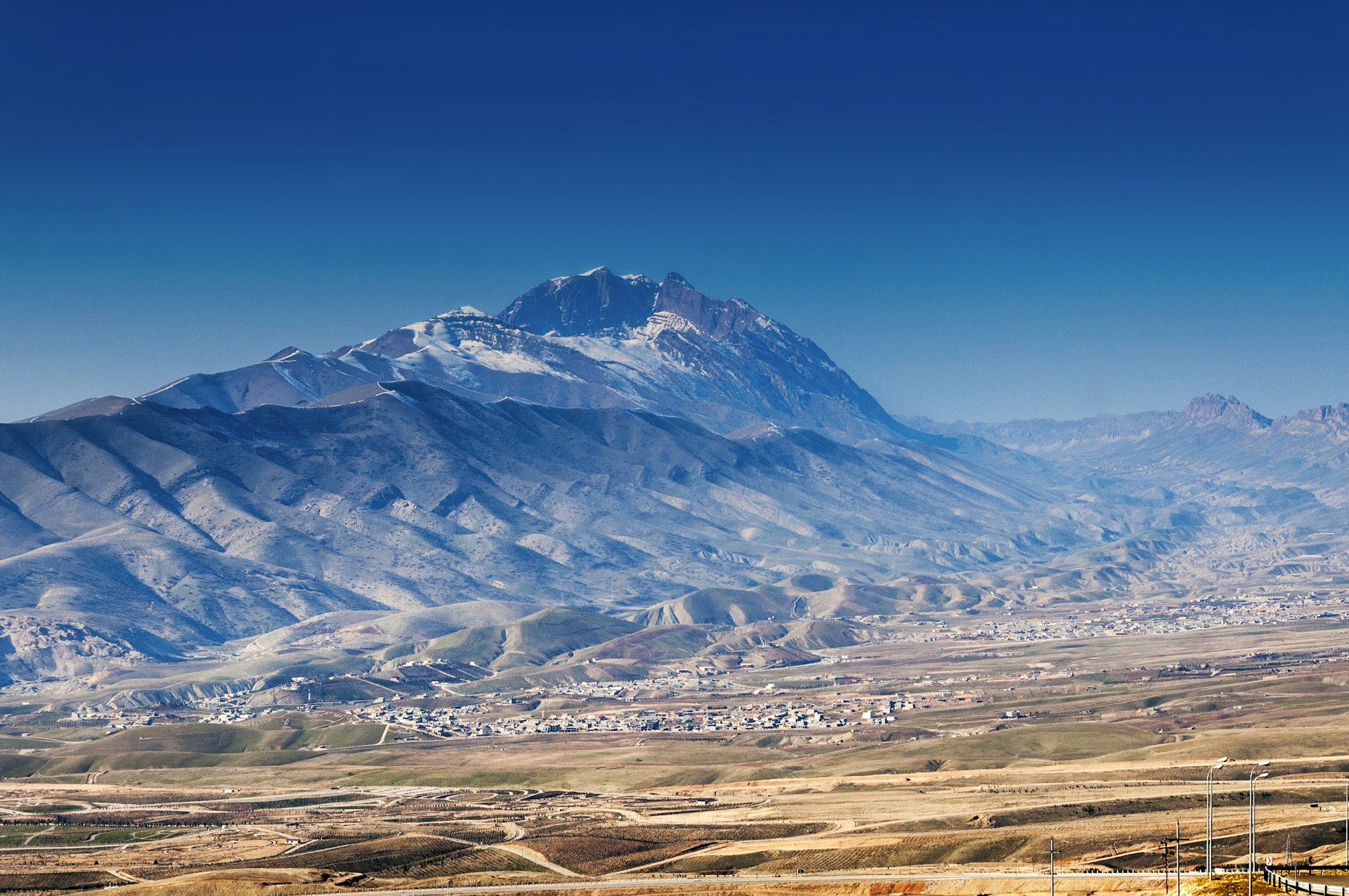 A huge mountain rises above a tiny village in the foothills: Zagros Mountains