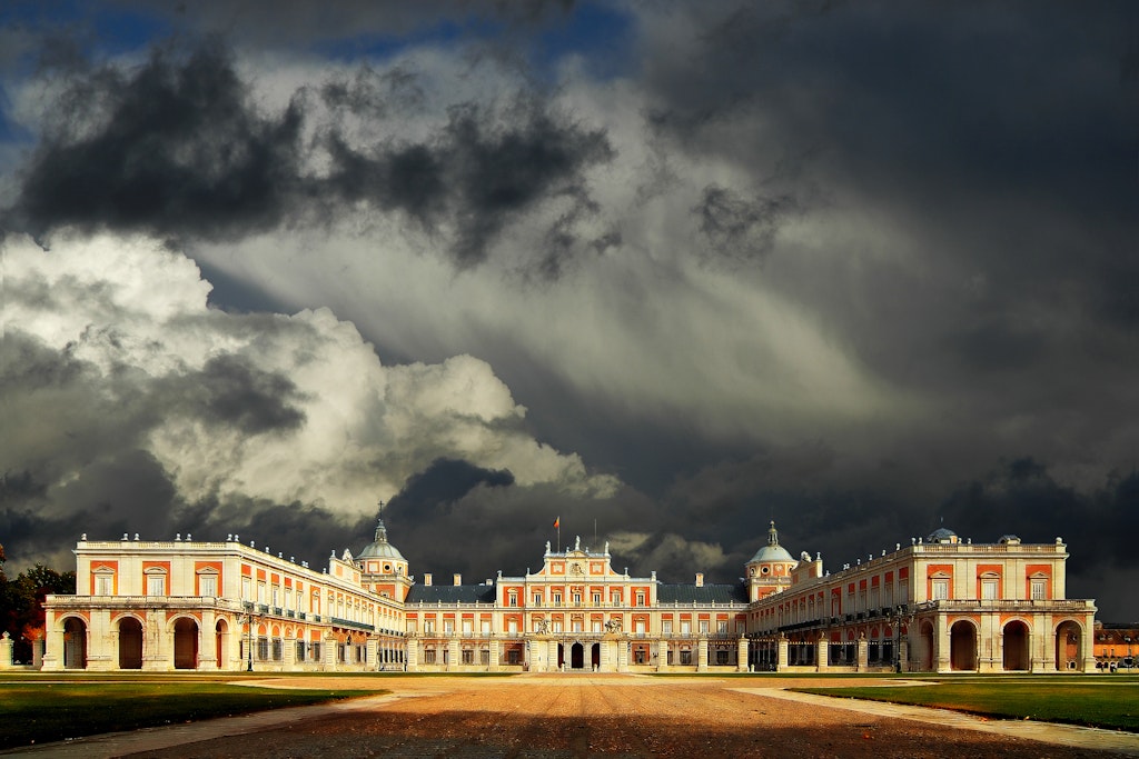 A red-and white brick palace building under a grey cloudy sky that threatens storms