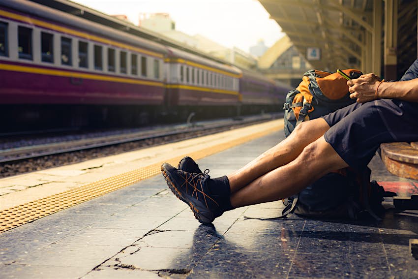 Backpacker using mobile phone in railway station while waiting for train.