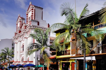 Palm trees in front of colourful buildings and the Church Of Our Lady Of Carmen in Guatapé.