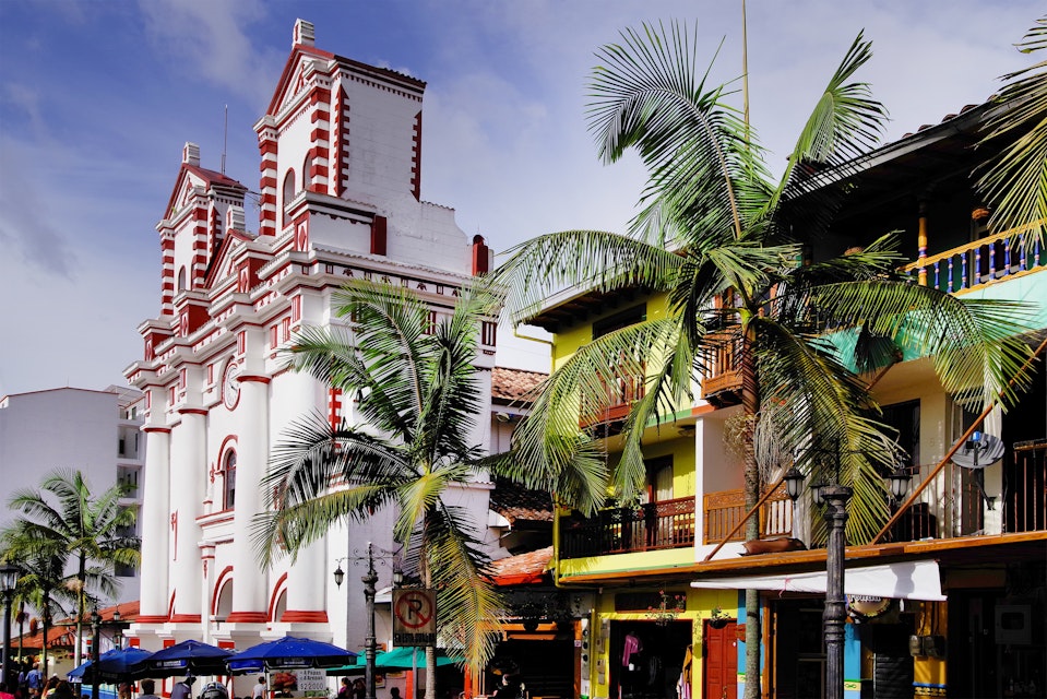 Palm trees in front of colourful buildings and the Church Of Our Lady Of Carmen in Guatapé.