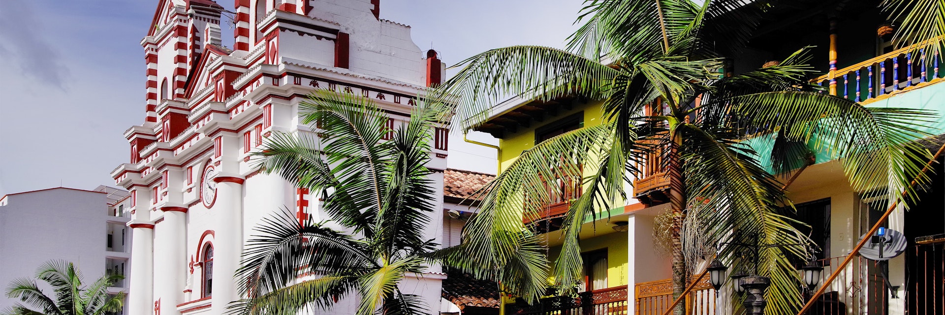 Palm trees in front of colourful buildings and the Church Of Our Lady Of Carmen in Guatapé.