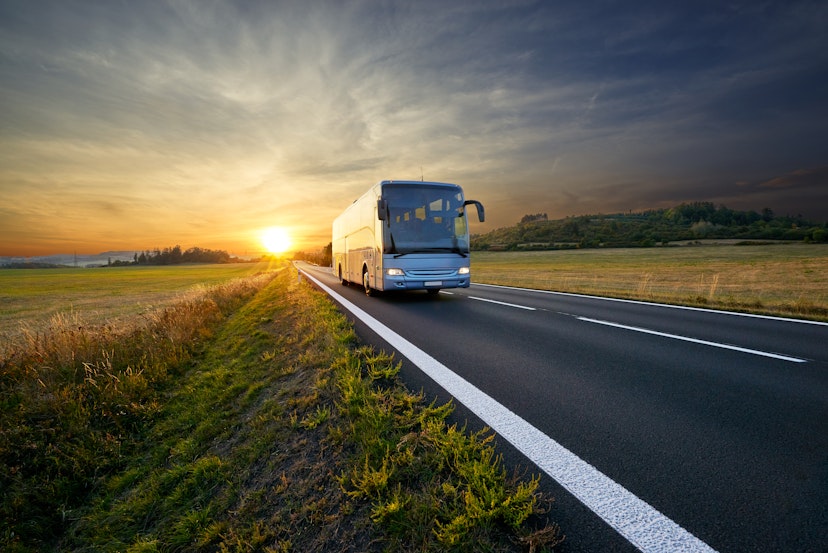 Bus traveling on an asphalt road in a rural area of Czech Republic during sunset.