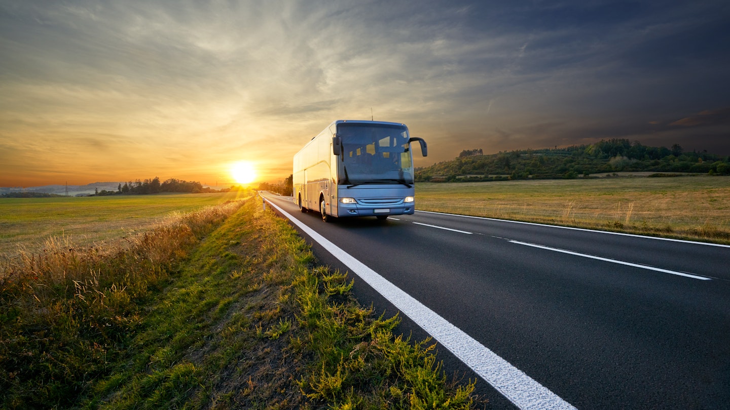 Bus traveling on an asphalt road in a rural area of Czech Republic during sunset.