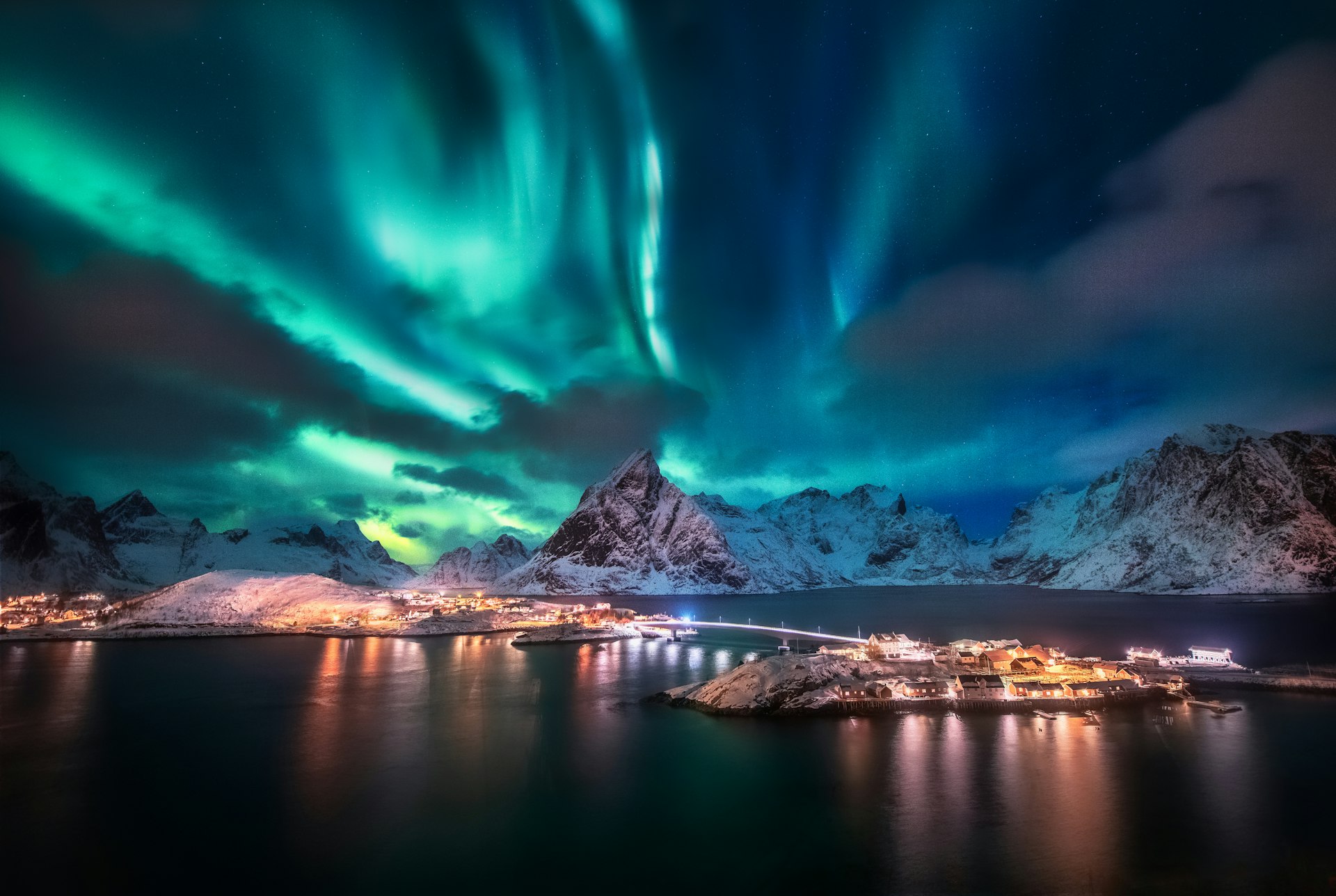The green Aurora Borealis streak across the dark sky above the Lofoten Islands in Norway. A snowy mountainscape is visible beneath the light show.