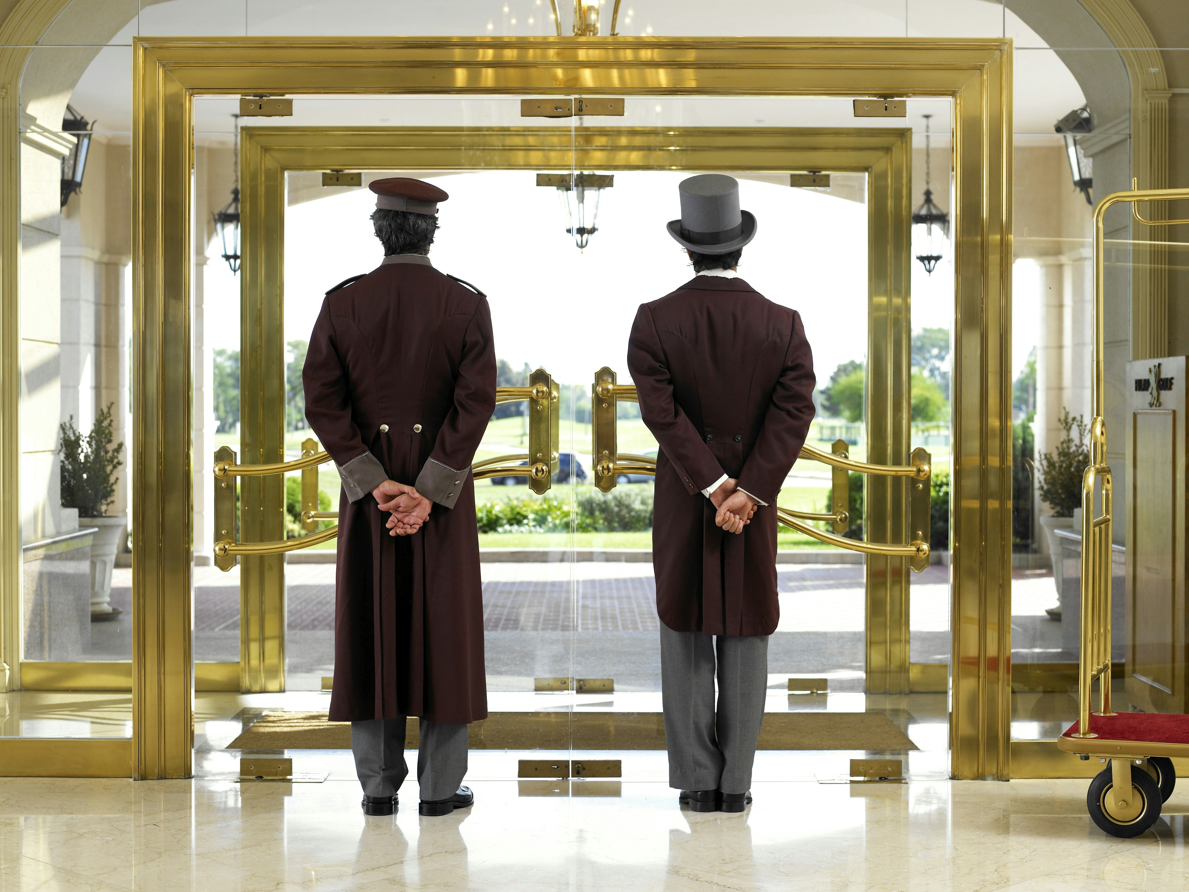 Concierge and bellboy standing at a hotel entrance and looking out the door.