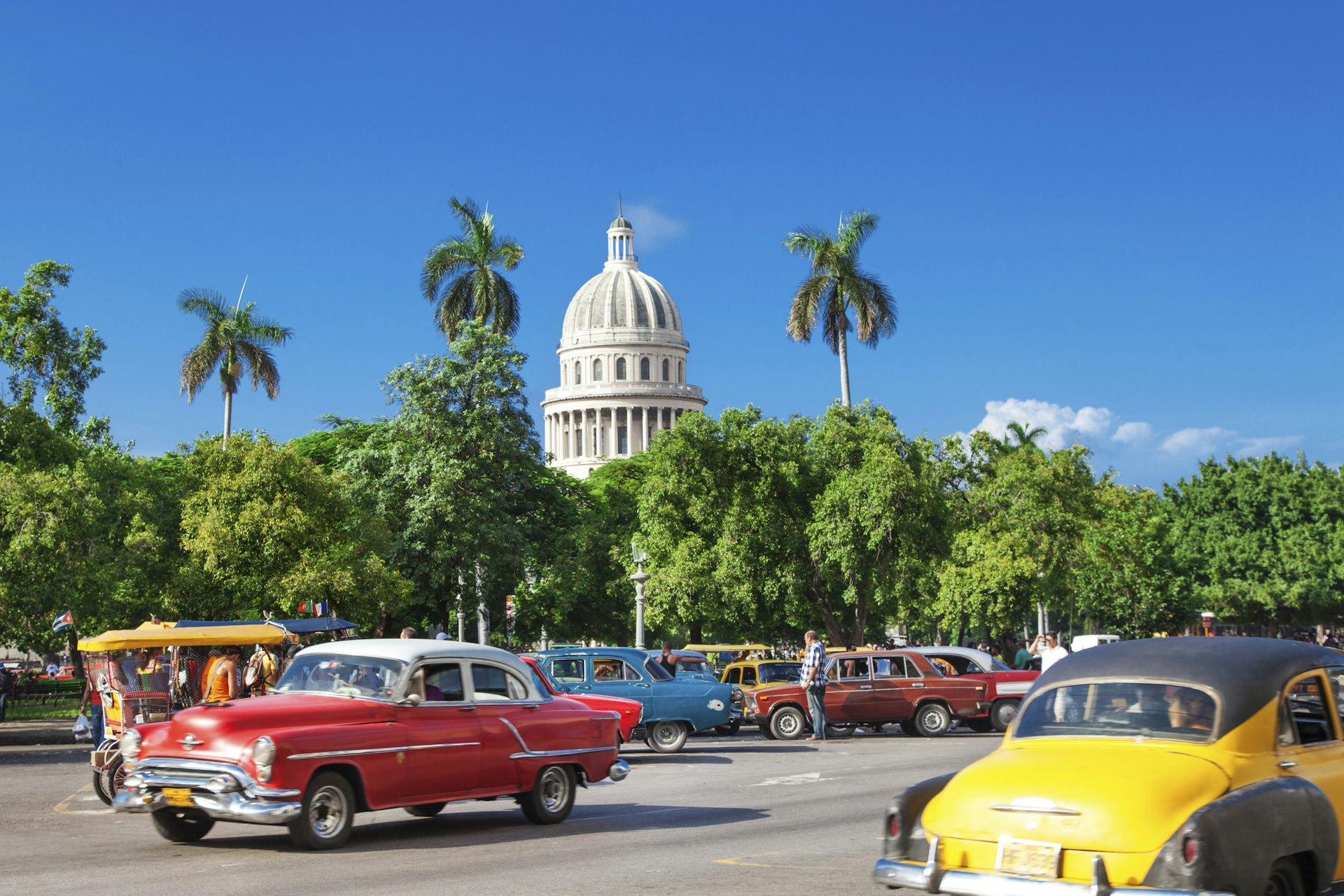 The dome of El Capitolio stands above trees and vintage cars