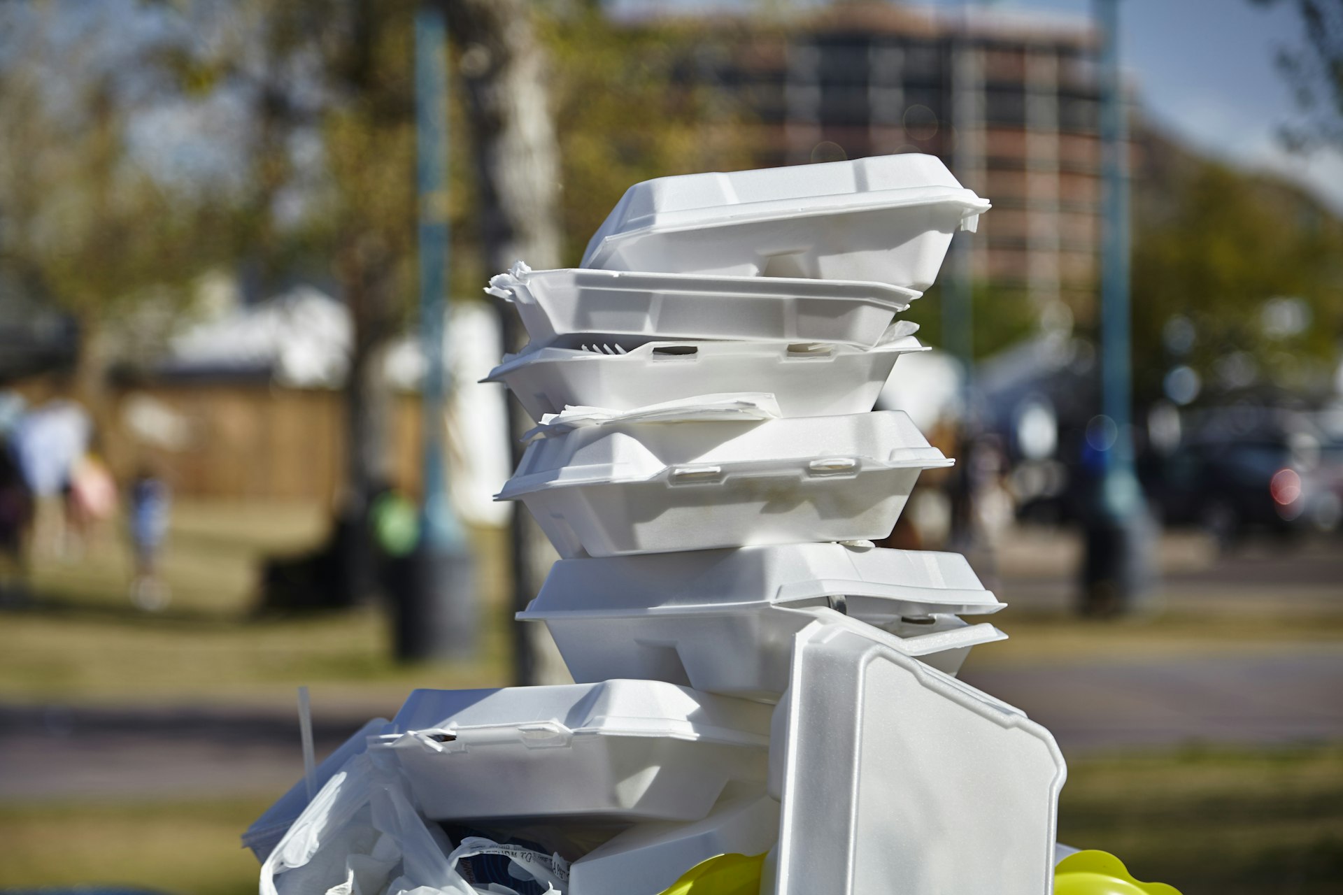 Used white fast-food containers piled on top of a trash can