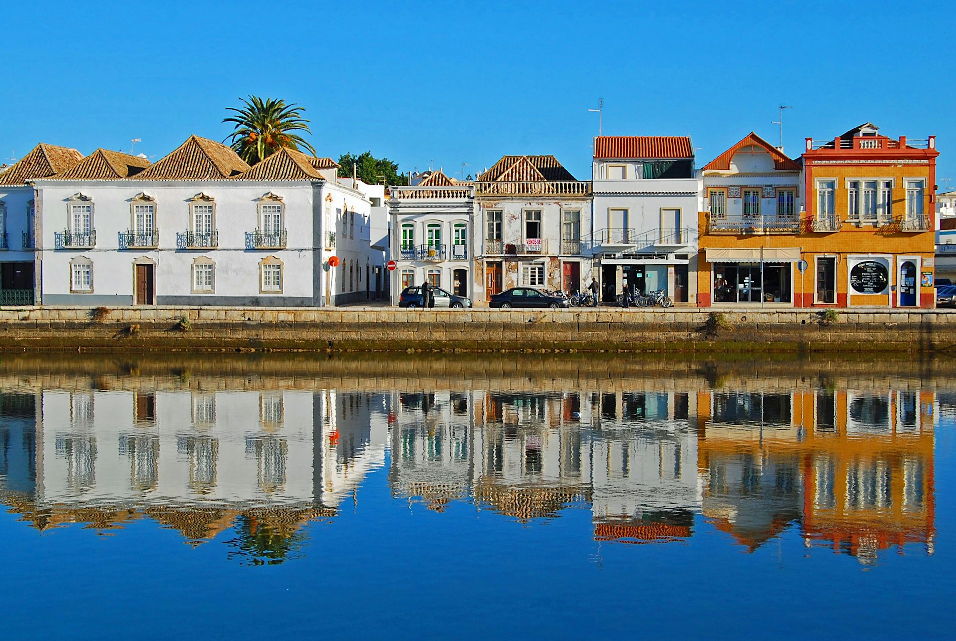 White and orange houses line a waterfront and are reflected in the water