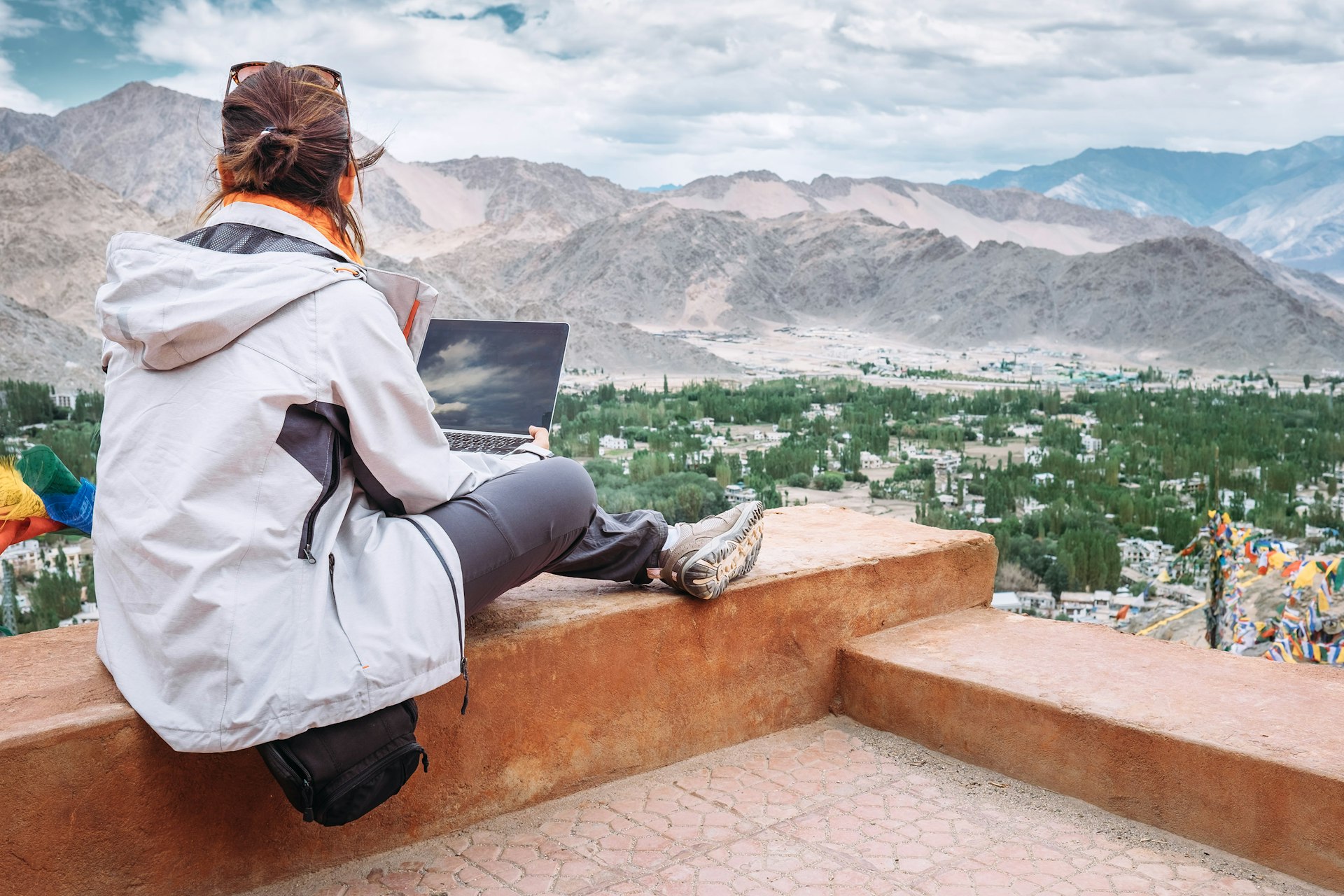 Traveler with laptop sits on top view point on the mountain valley