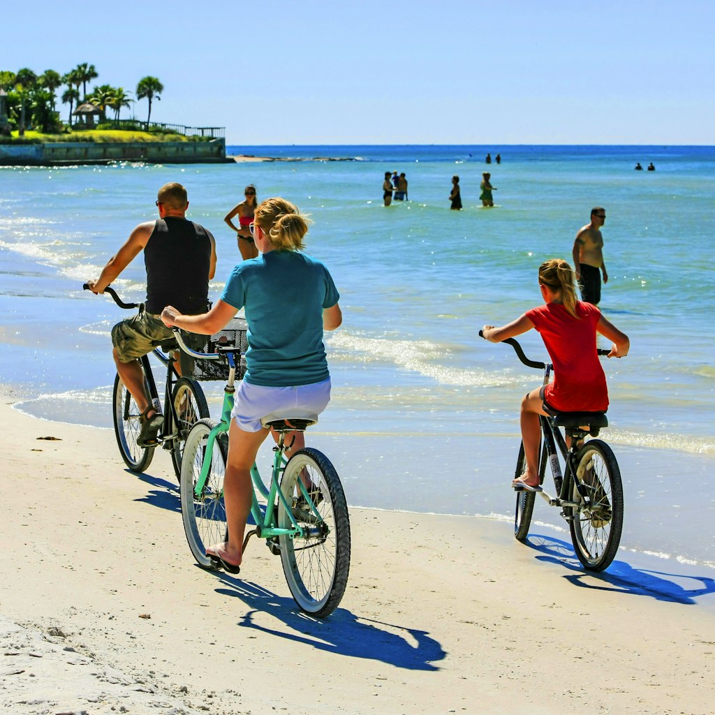 Family group riding beach cruiser bicycles along Crescent beach on Siesta Key, Sarasota FL USA