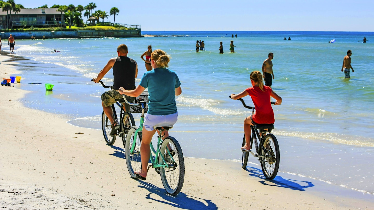 Family group riding beach cruiser bicycles along Crescent beach on Siesta Key, Sarasota FL USA
