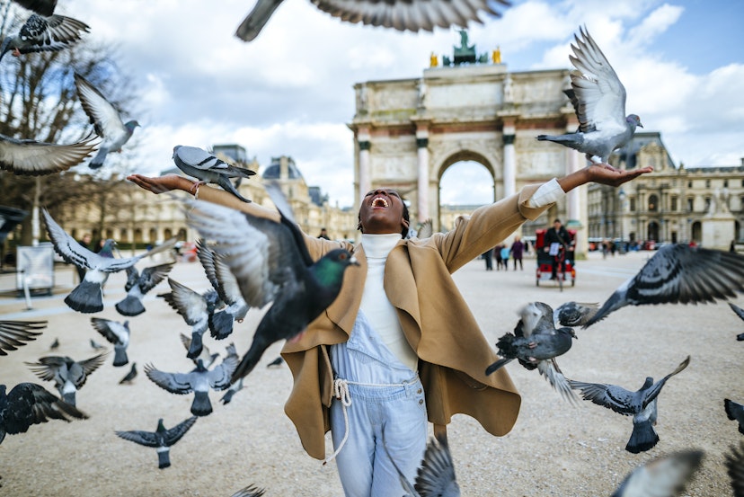 France, Paris, Happy young woman with flying pidgeons at Arc de Triomphe