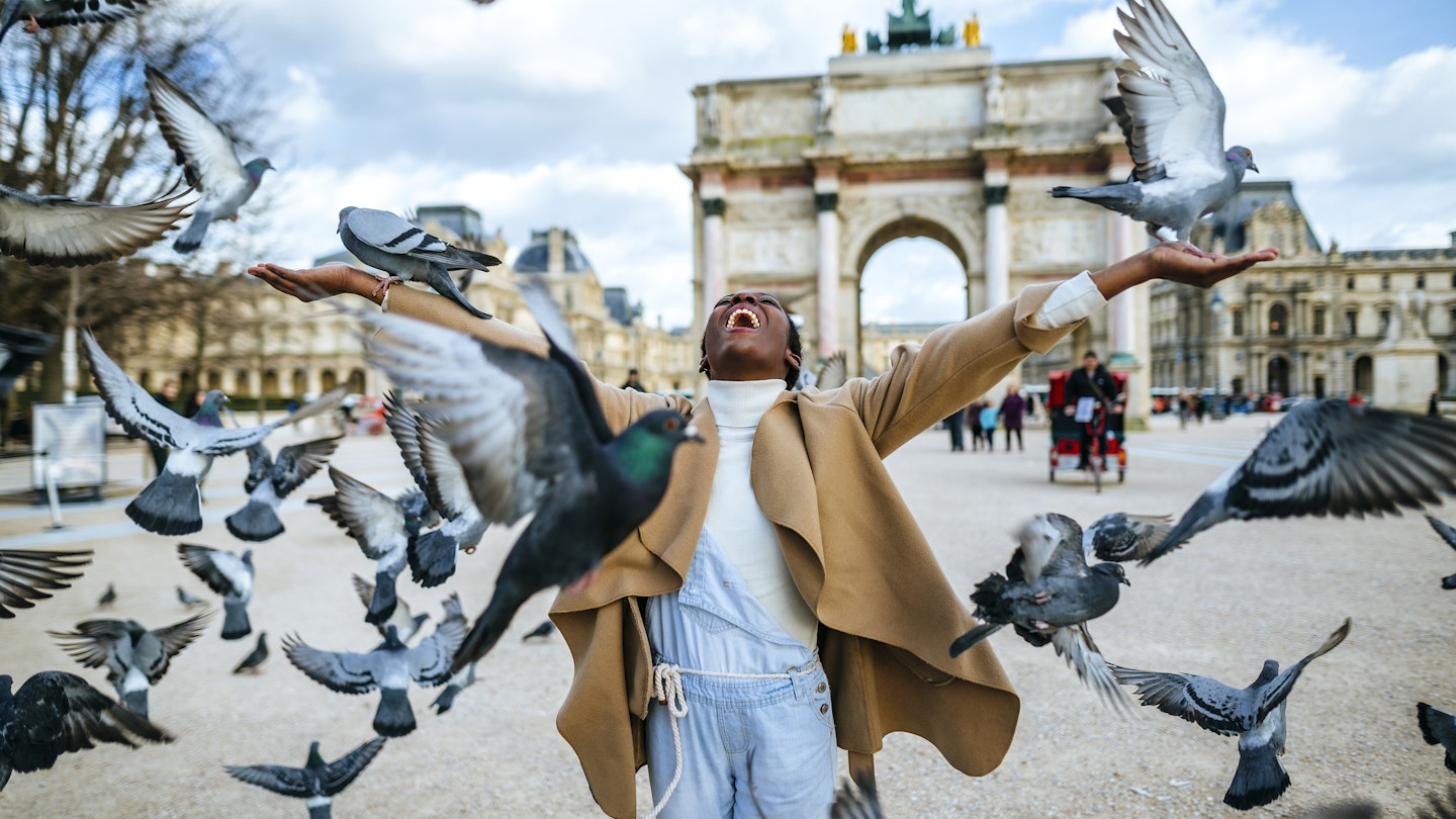 France, Paris, Happy young woman with flying pidgeons at Arc de Triomphe
