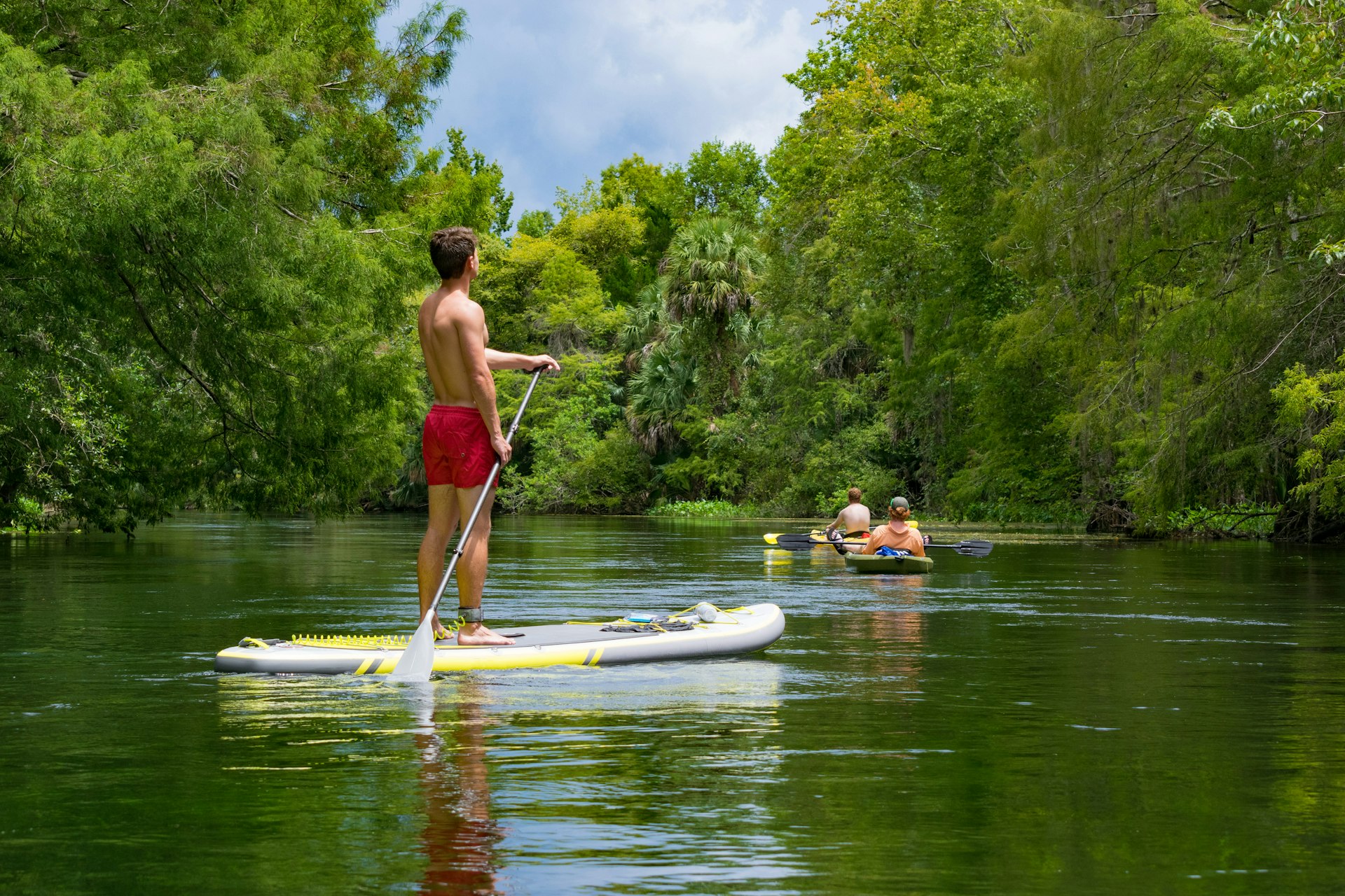 A male standup paddleboarder and two kayakers go down a river
