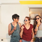 Three friends enjoying ice creams while standing against a campervan.