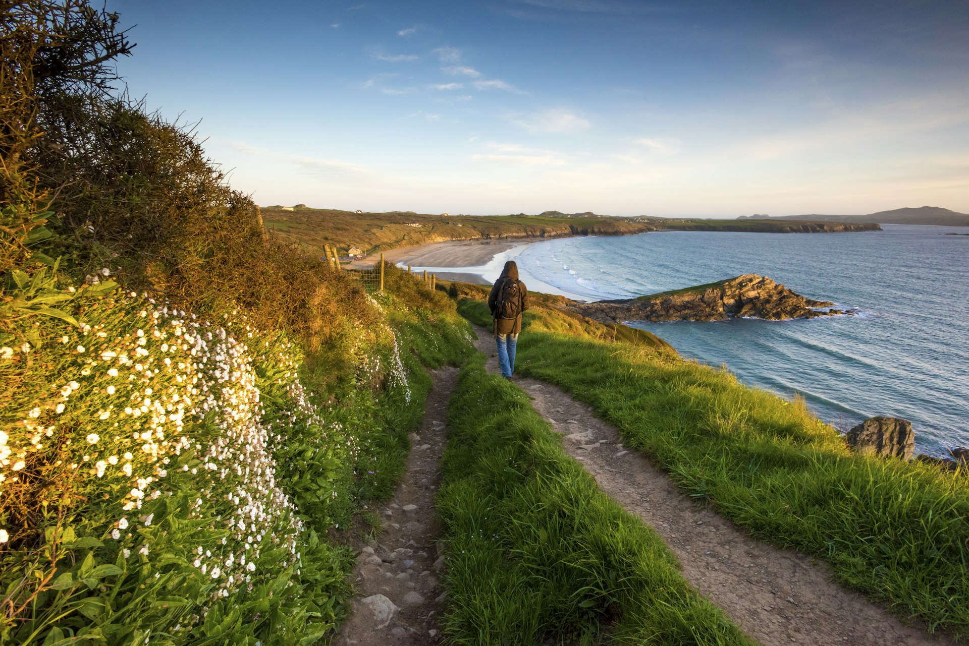 A walker follows a rustic Welsh coastline. 