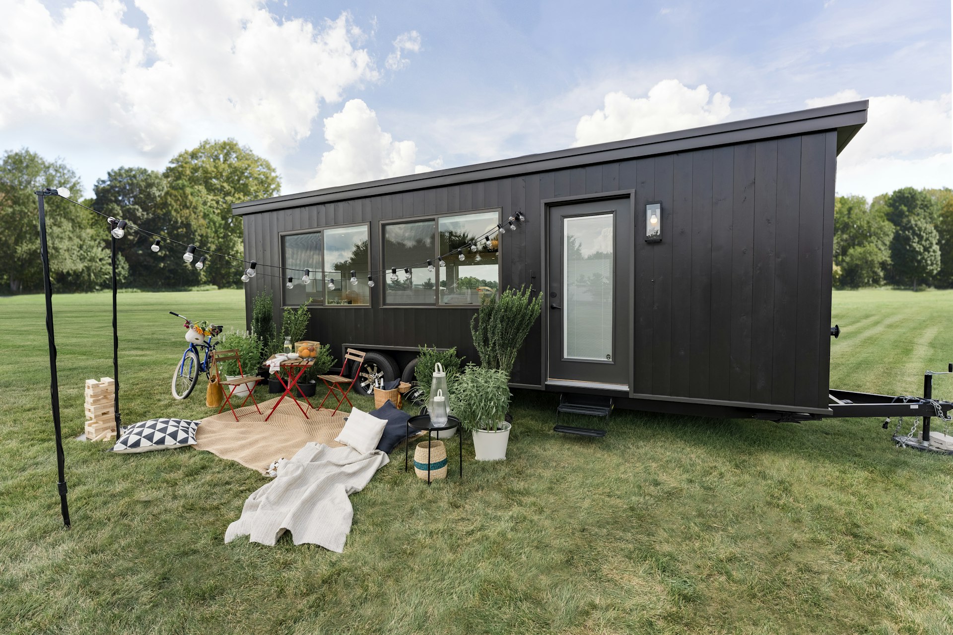 Exterior shot of a panel-clad tiny home in a field with a picnic space outside