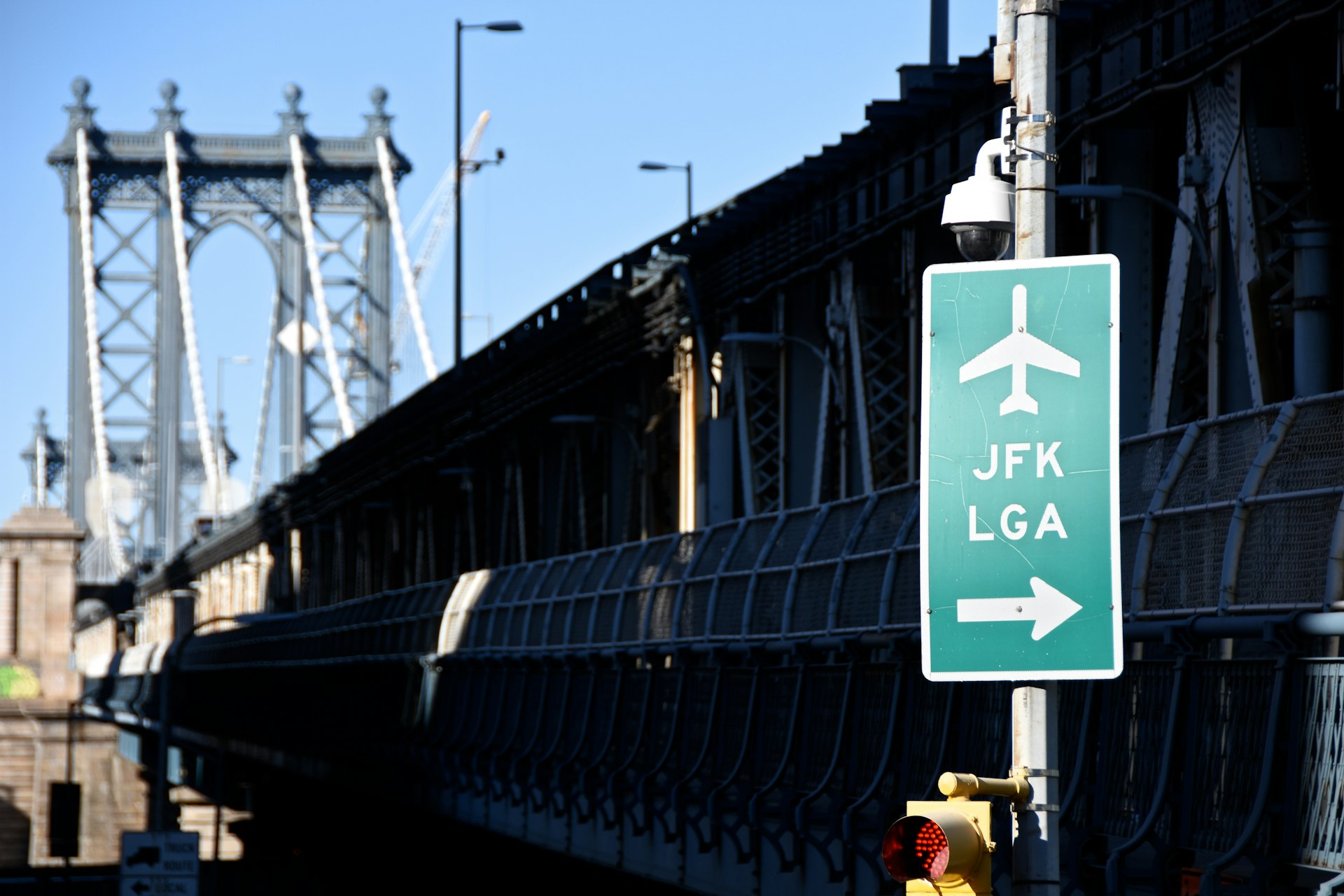A green road sign for JFK and LaGuardia airports with a bridge and skyline in the background