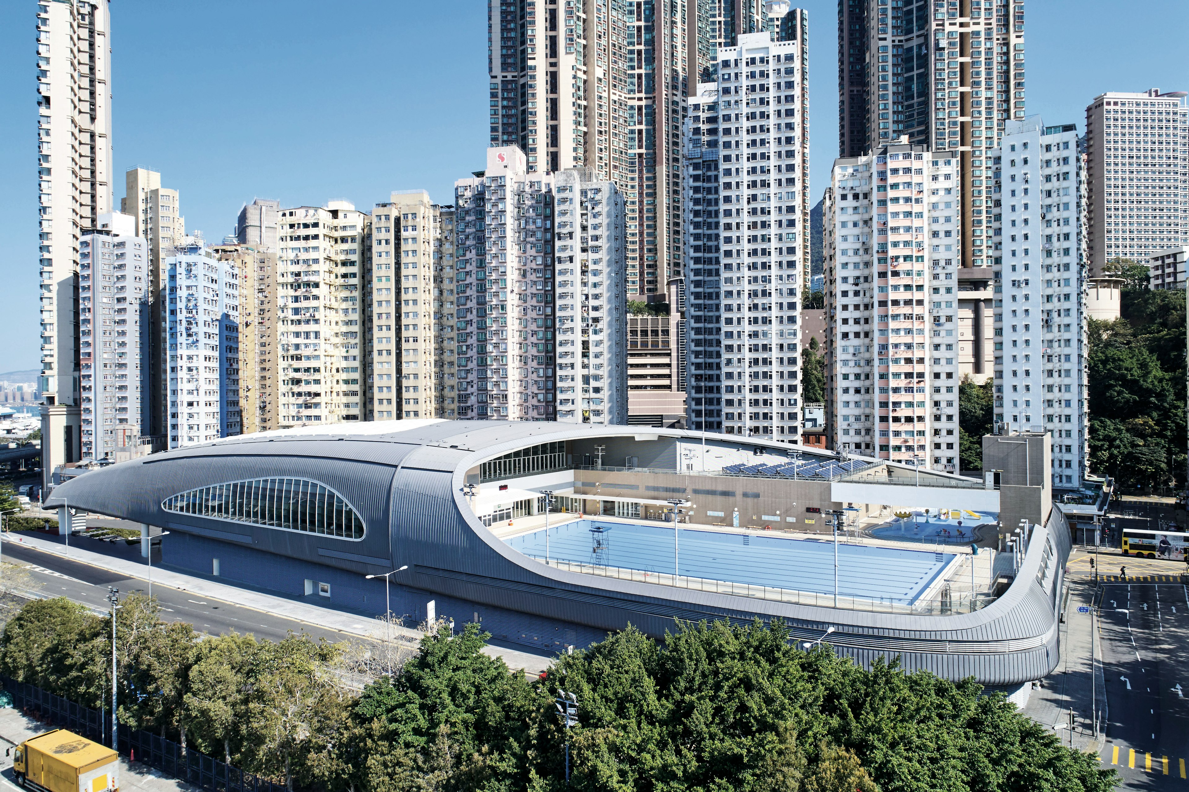 A large open-air pool as part of a futuristic-looking complex. The pool is overlooked by tall apartment buildings