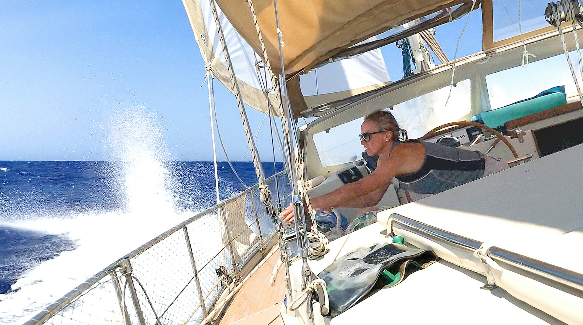 A woman leans away from the wheel of the boat to adjust some ropes as it sails through the sea