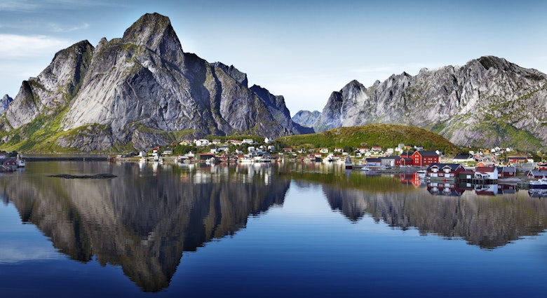 Dramatic granite peaks of Lofoten Wall and Reinebringen reflected in water beside fishing village of Reine.