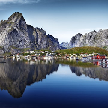 Dramatic granite peaks of Lofoten Wall and Reinebringen reflected in water beside fishing village of Reine.