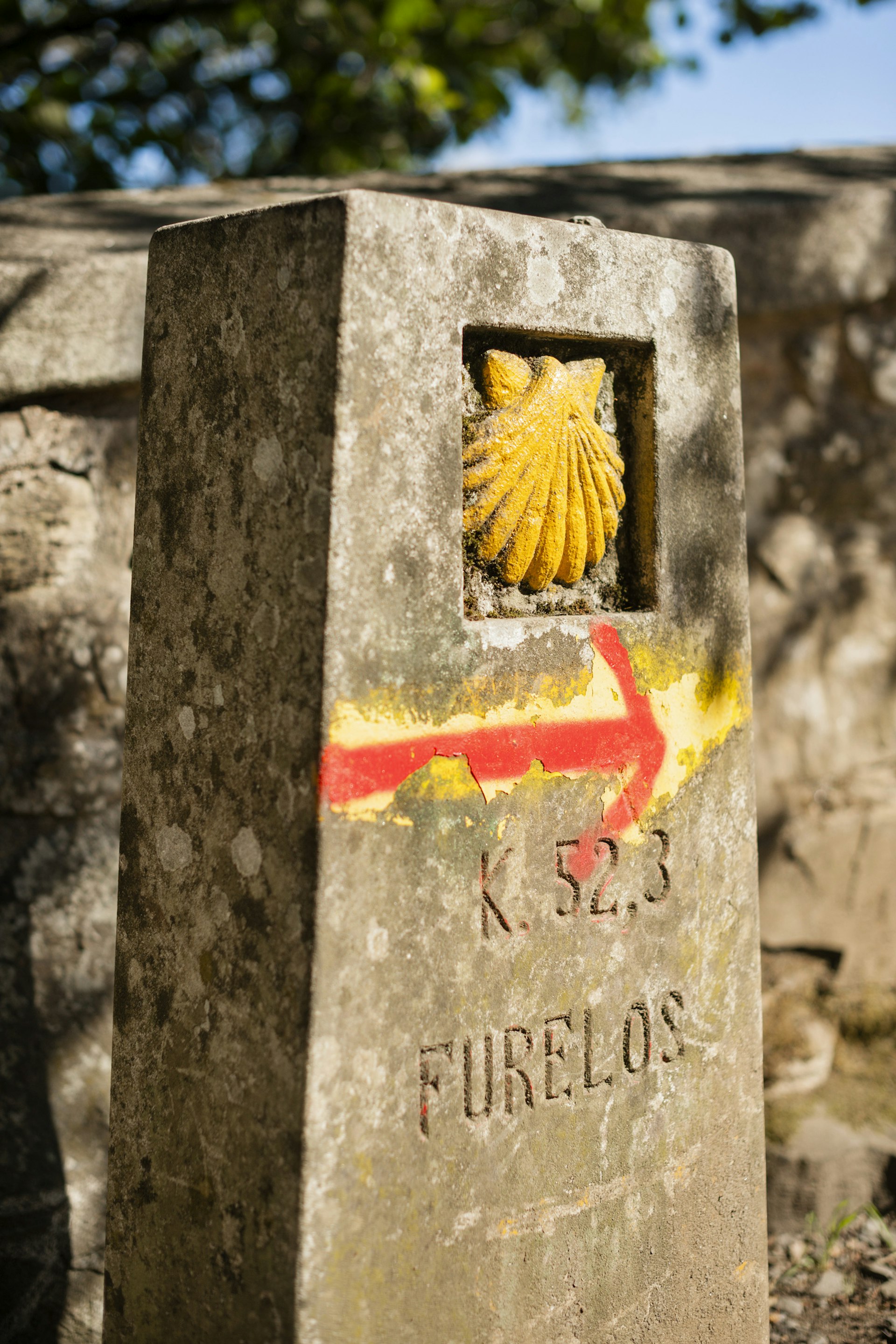 Shot of a golden scallop shell on a small stone pillar. The scallop is the symbol of the Camino