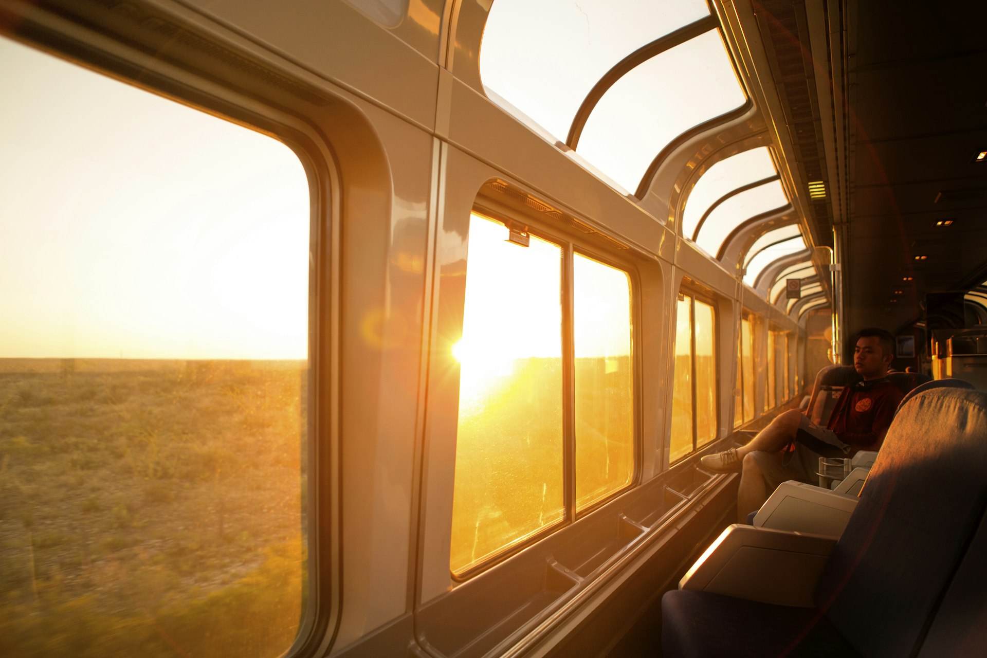 A young man watches the sun rise over the Texas landscape through the large windows of the Amtrack train travelling from San Antonio to Alpine.