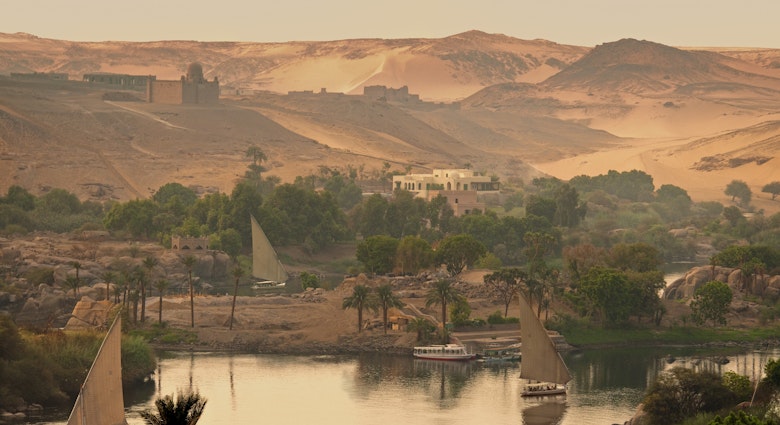 Felucca boats sailing on the Nile River. The Aga Khan’s domed mausoleum sits on the hill in the background.
