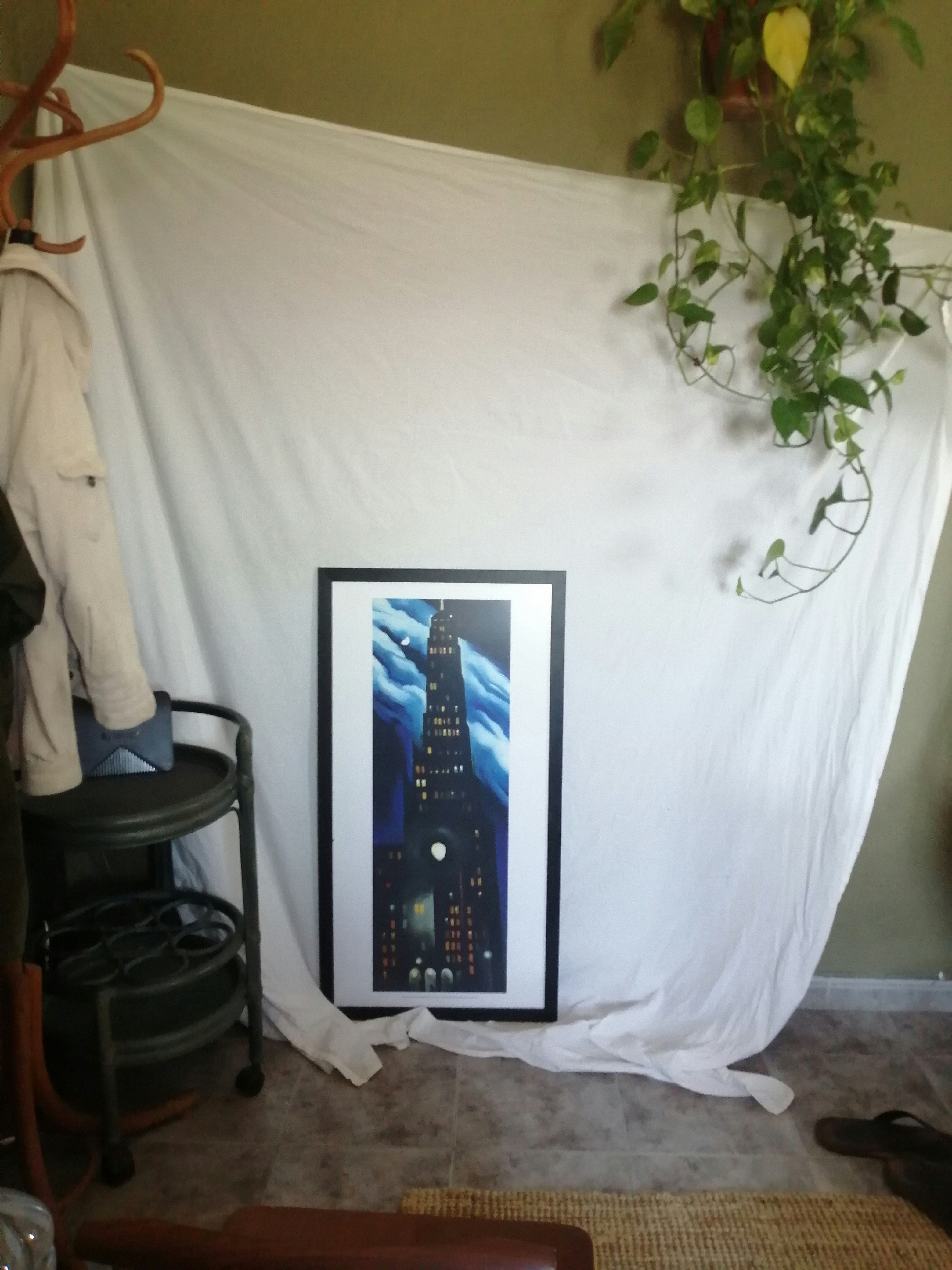 A white sheet hangs on a wall with a painting by Georgia O'Keeffe (a skyscraper at night) propped up against it