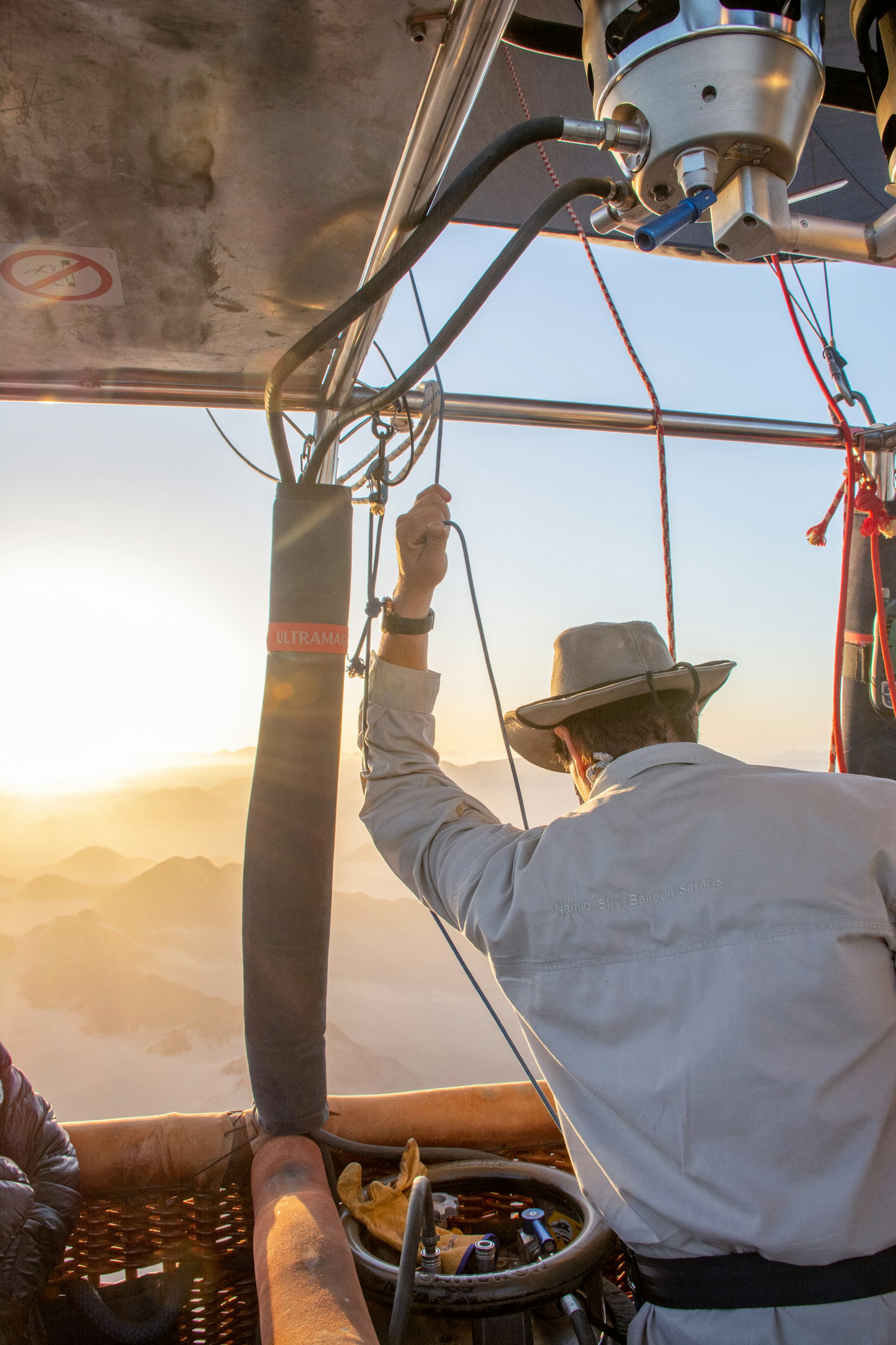 A man controls a hot air balloon while looking down over a mountain range