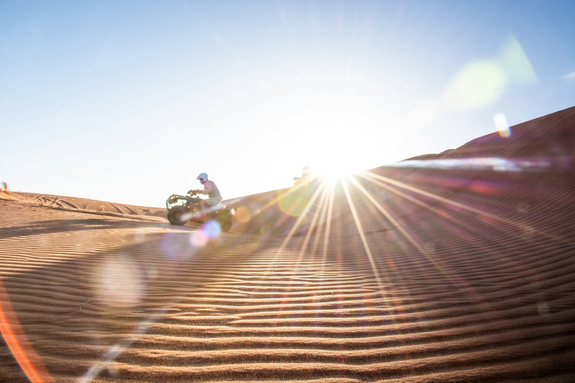 A quad bike travels over sand dunes 