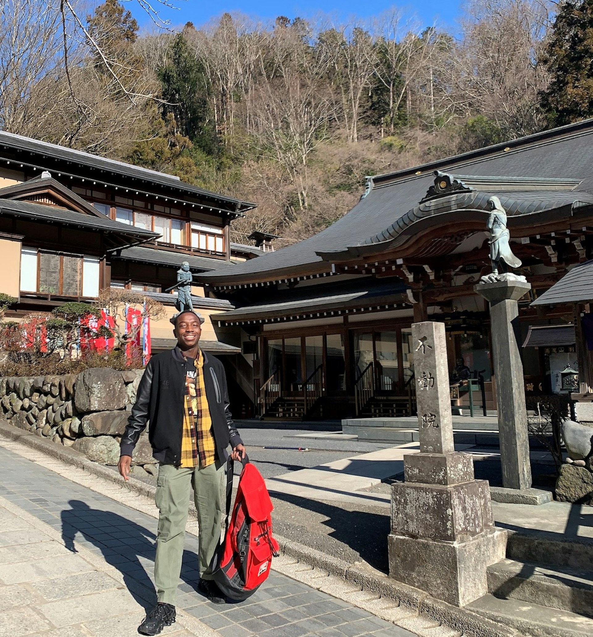 A black man stands outside traditional Japanese architecture and smiles for the camera