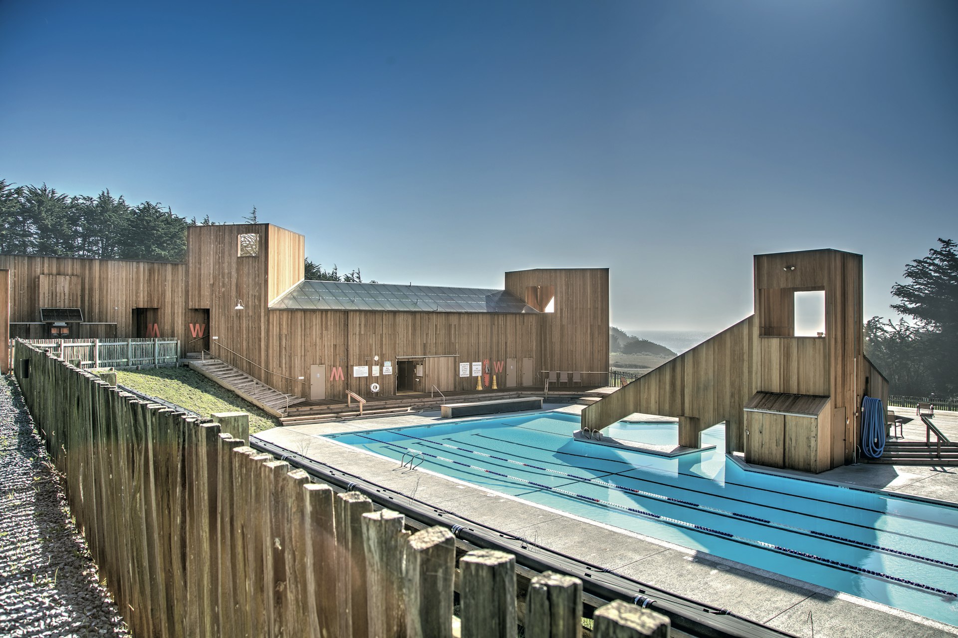 A rooftop pool with a modern wooden building to one side, and a view to the distant ocean on the other