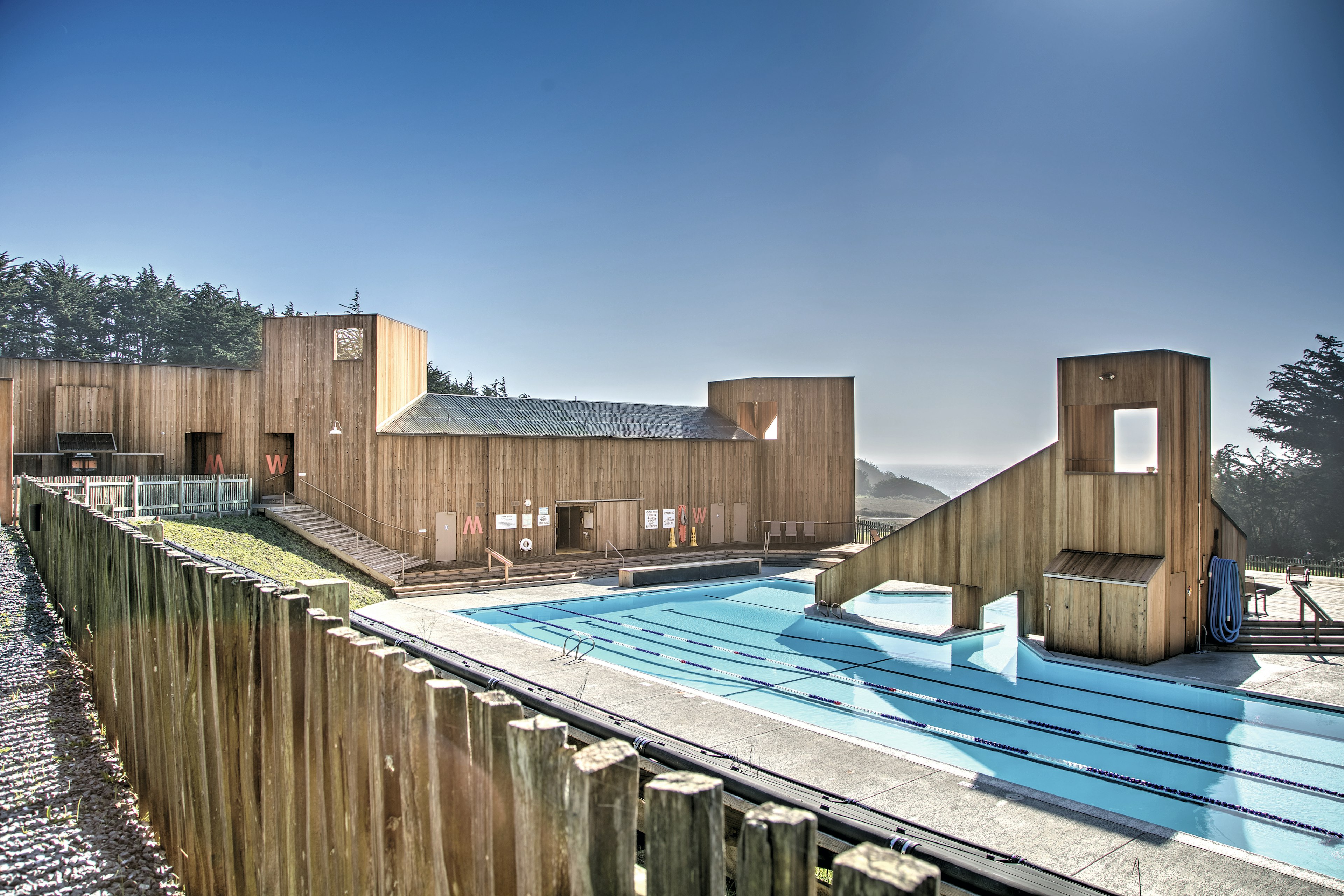 A rooftop pool with a modern wooden building to one side, and a view to the distant ocean on the other