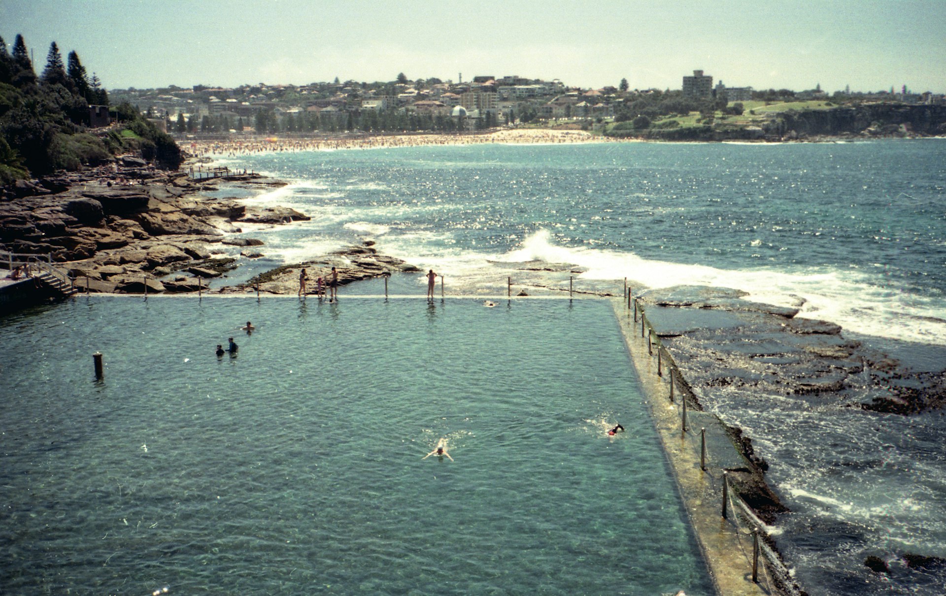 A swimming pool built just at wave level above the ocean, with a view over the sea towards a golden sand beach