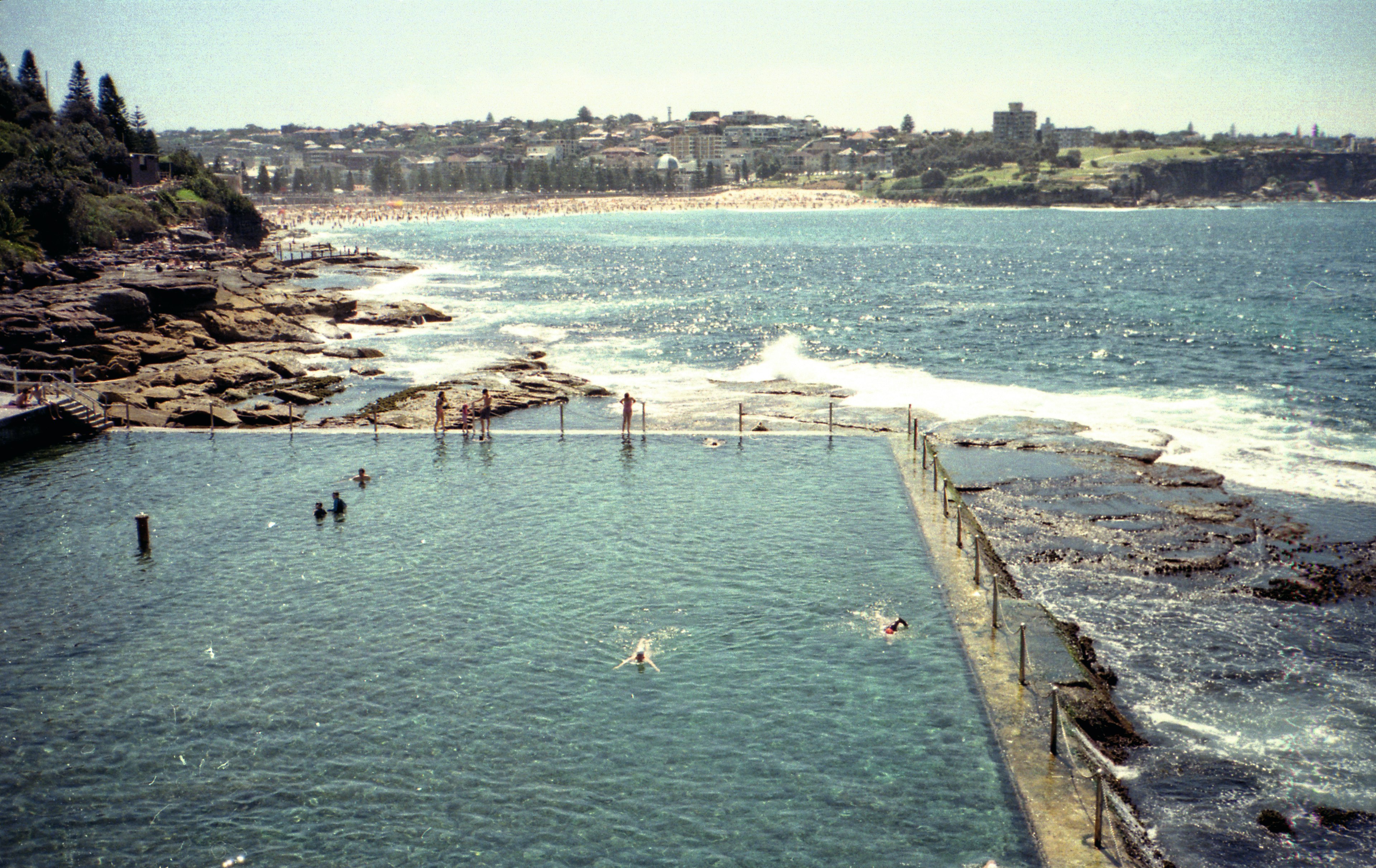 A swimming pool built just at wave level above the ocean, with a view over the sea towards a golden sand beach