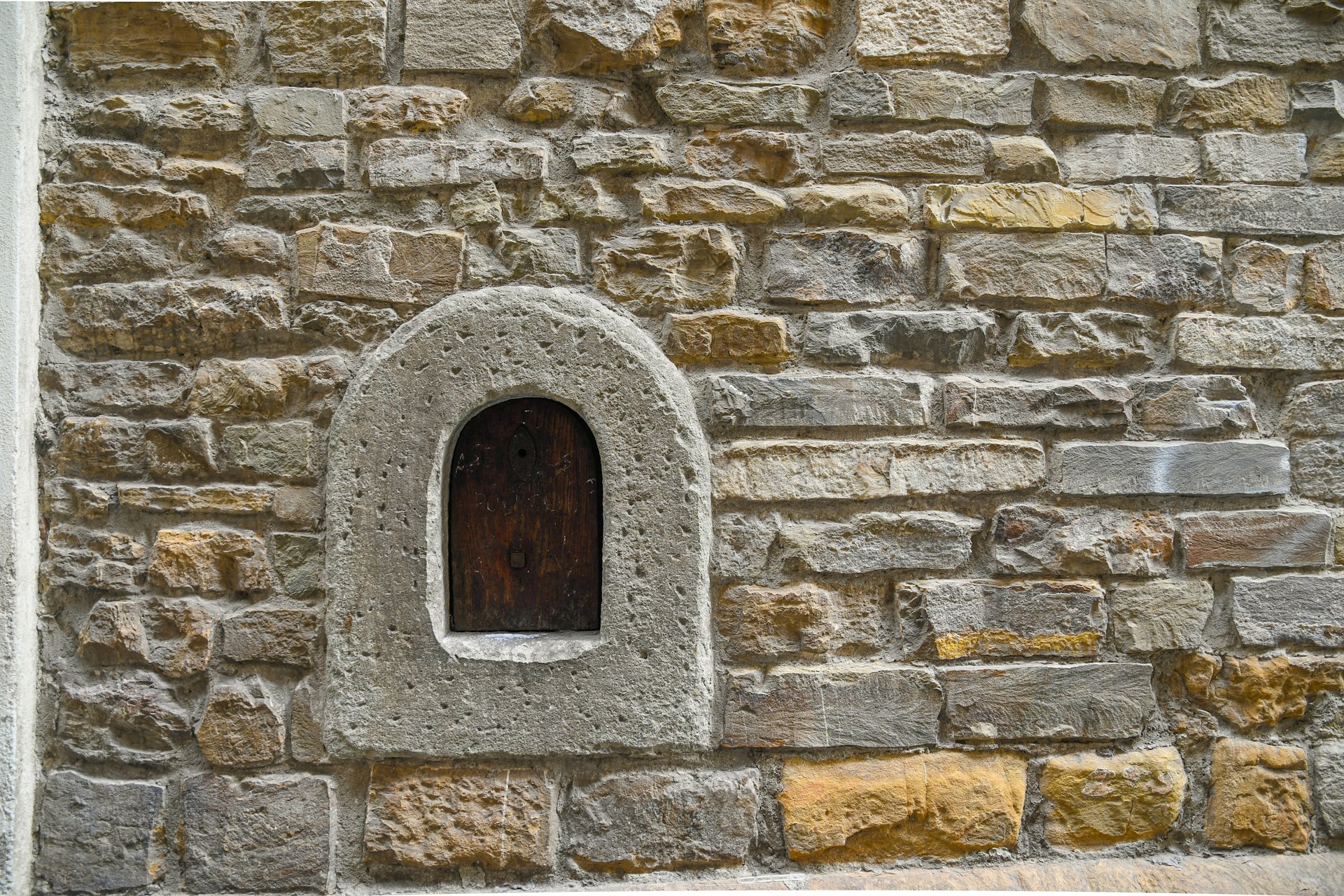 Close-up of a wine window (buchetta del vino), used in the past to sell wine directly to passers-by, on the old stone wall of an ancient building