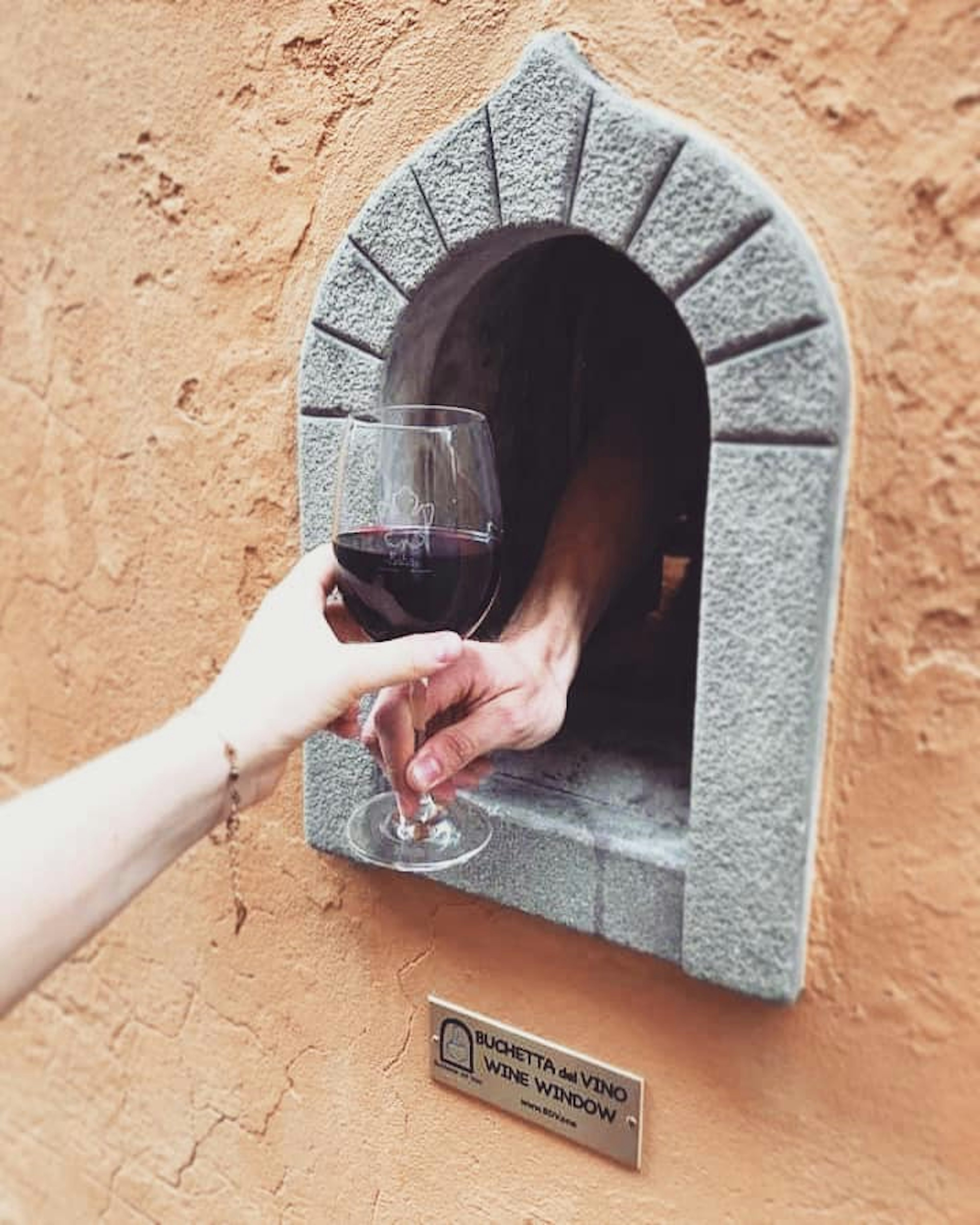 A glass of red wine is served to a passer-by from a wine window