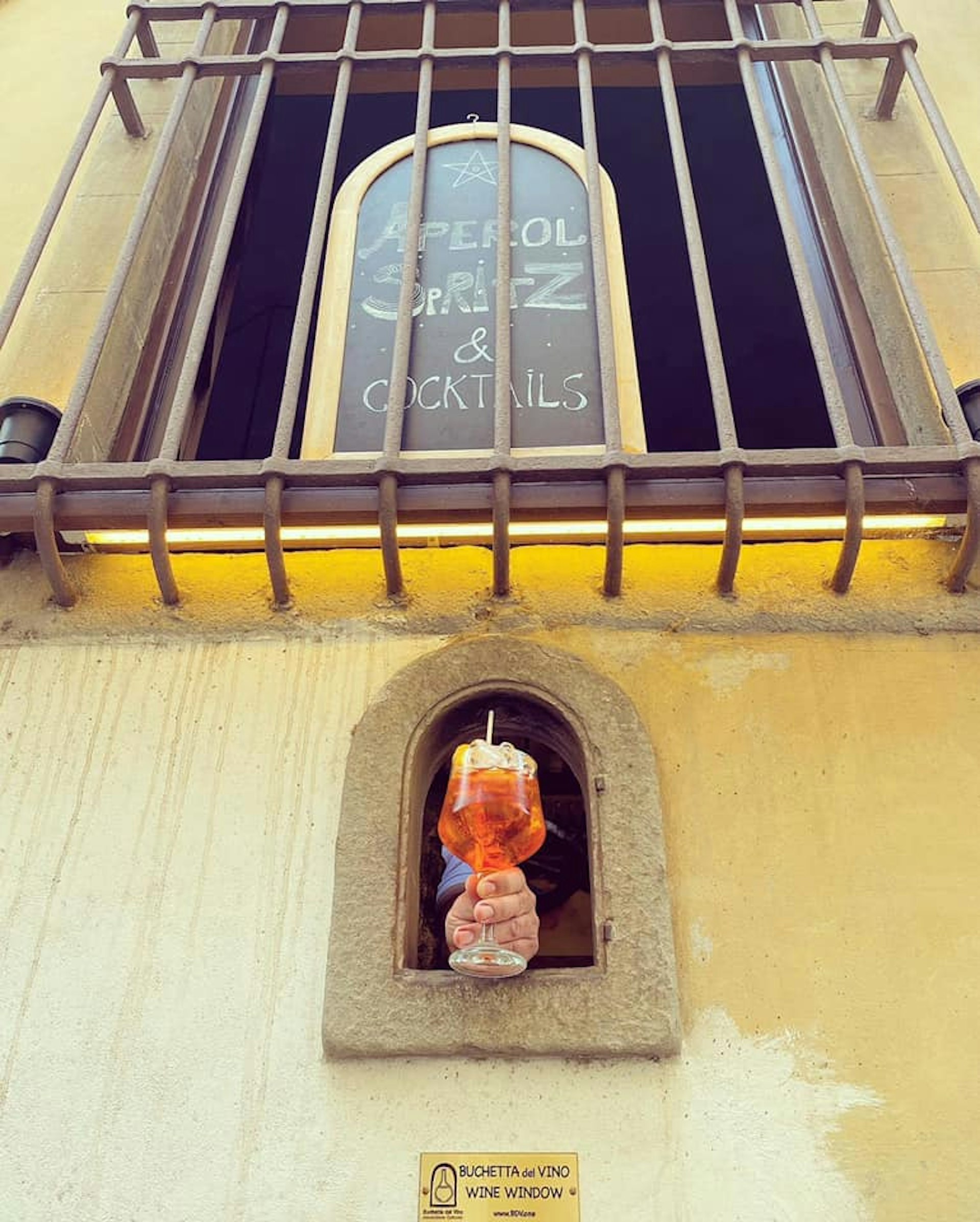 An Aperol Spritz is passed through a wine window in Florence